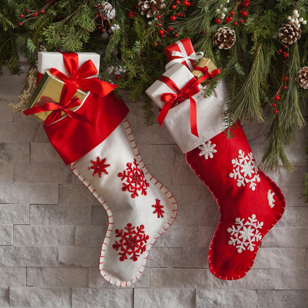 two stockings stuffed with gifts against a brick chimney with greenery