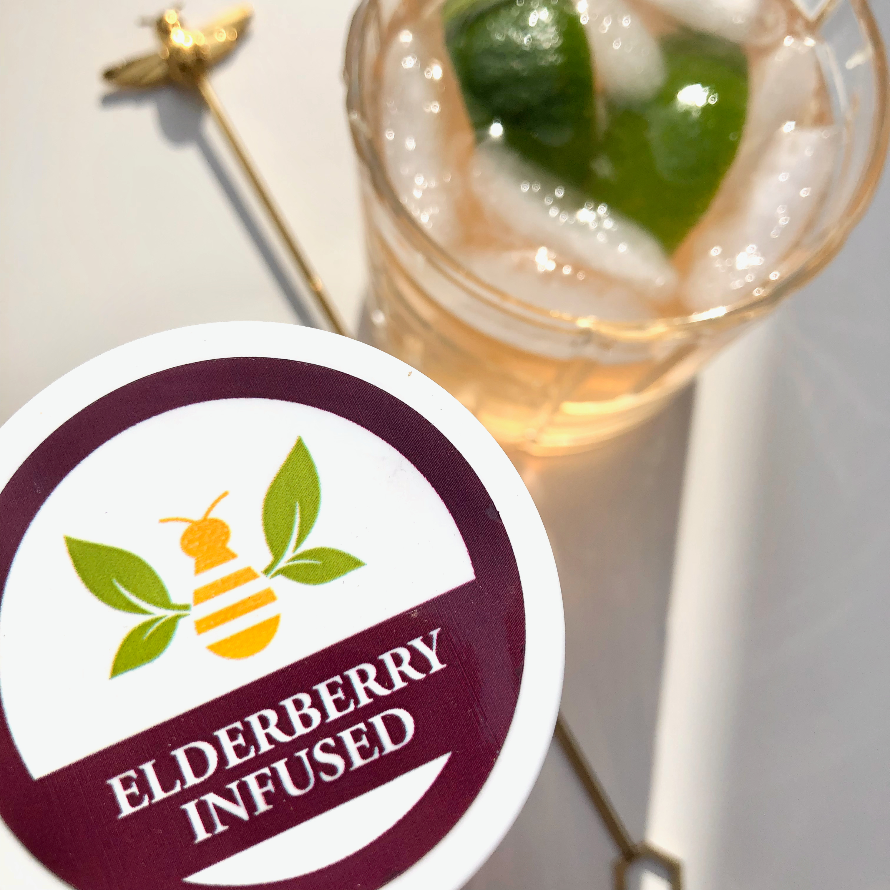 top down view of an elderberry honey g&t garnished with lime and the top of a jar of Elderberry Infused Honey from Saratoga Tea & Honey Co.