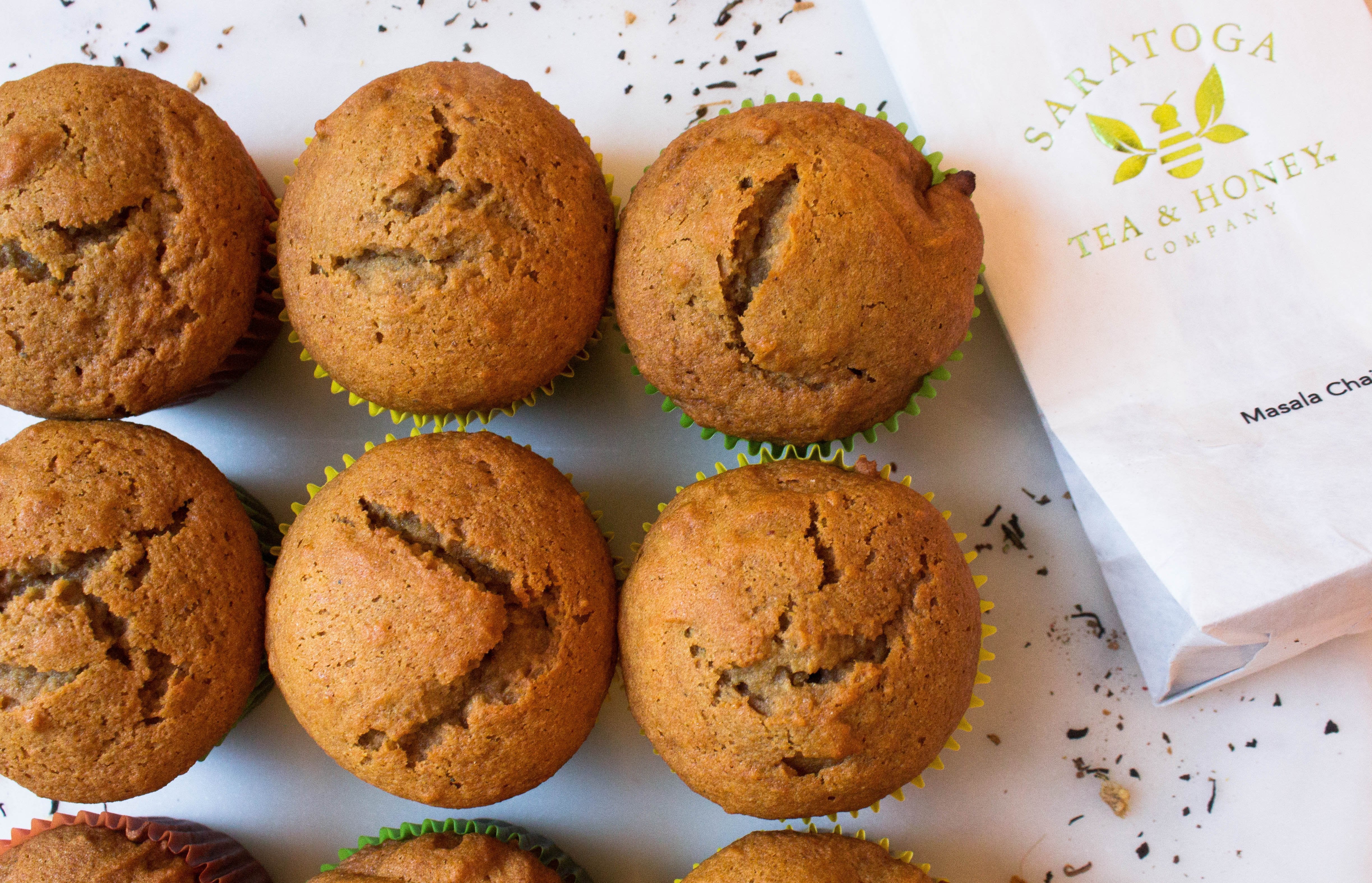 Six golden brown muffins next to a bag of Saratoga Tea & Honey Co. Masala Chai