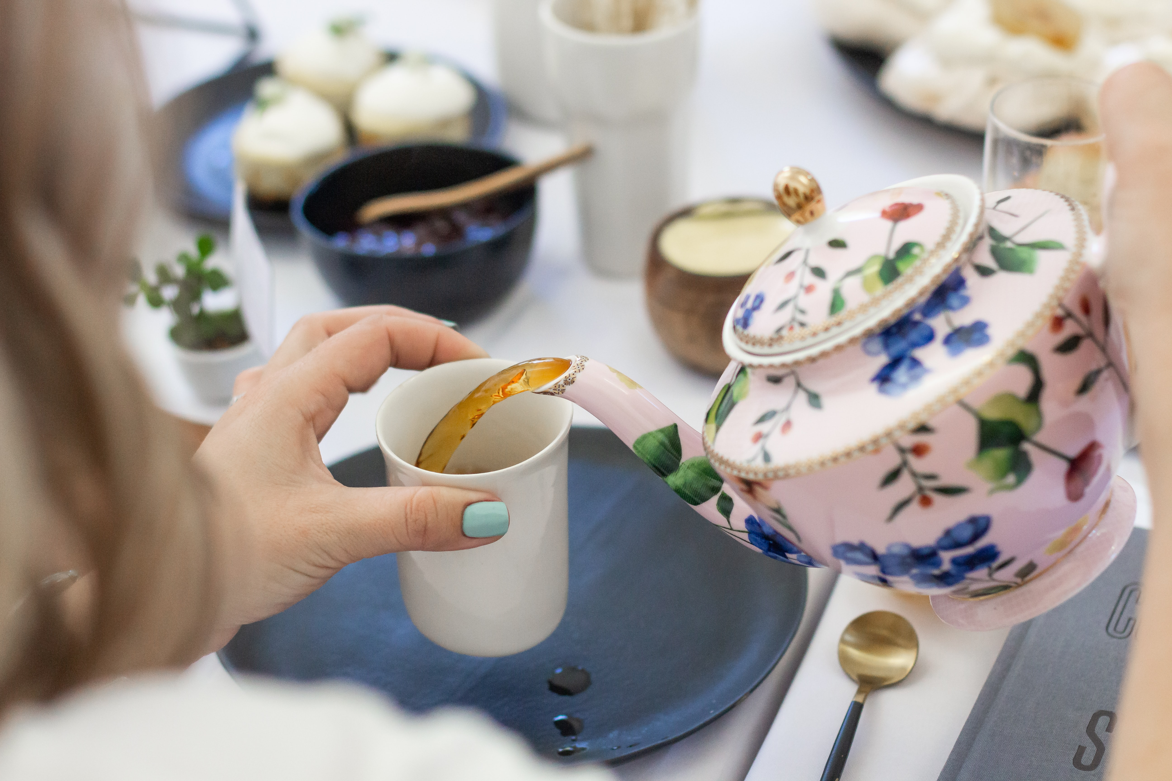 woman pouring tea into a cup from a porcelain teapot
