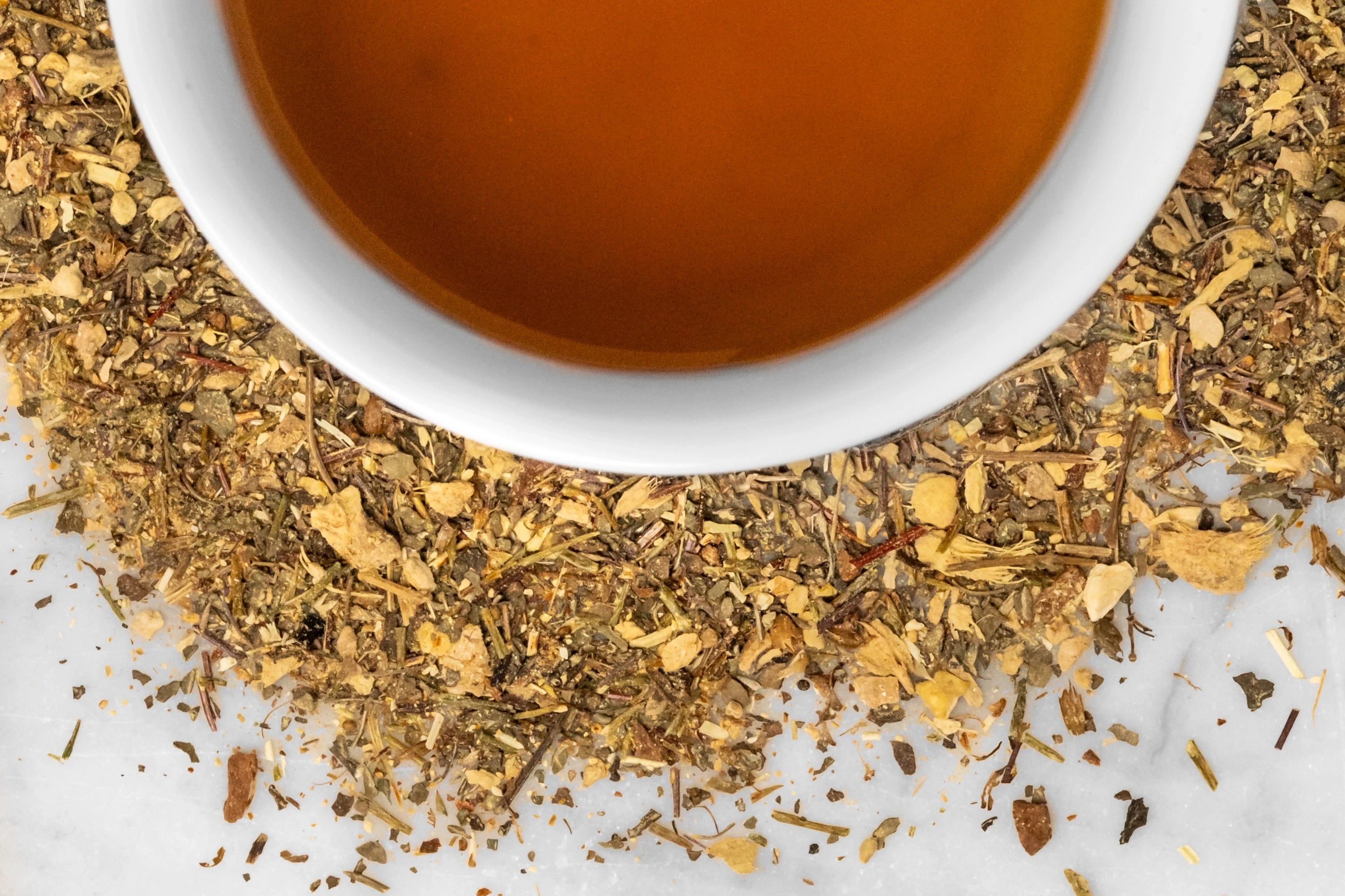 Awakening leaves and brewed tea. Dry, finely chopped mushrooms and herbs surround a cup of honey-brown brewed tea.