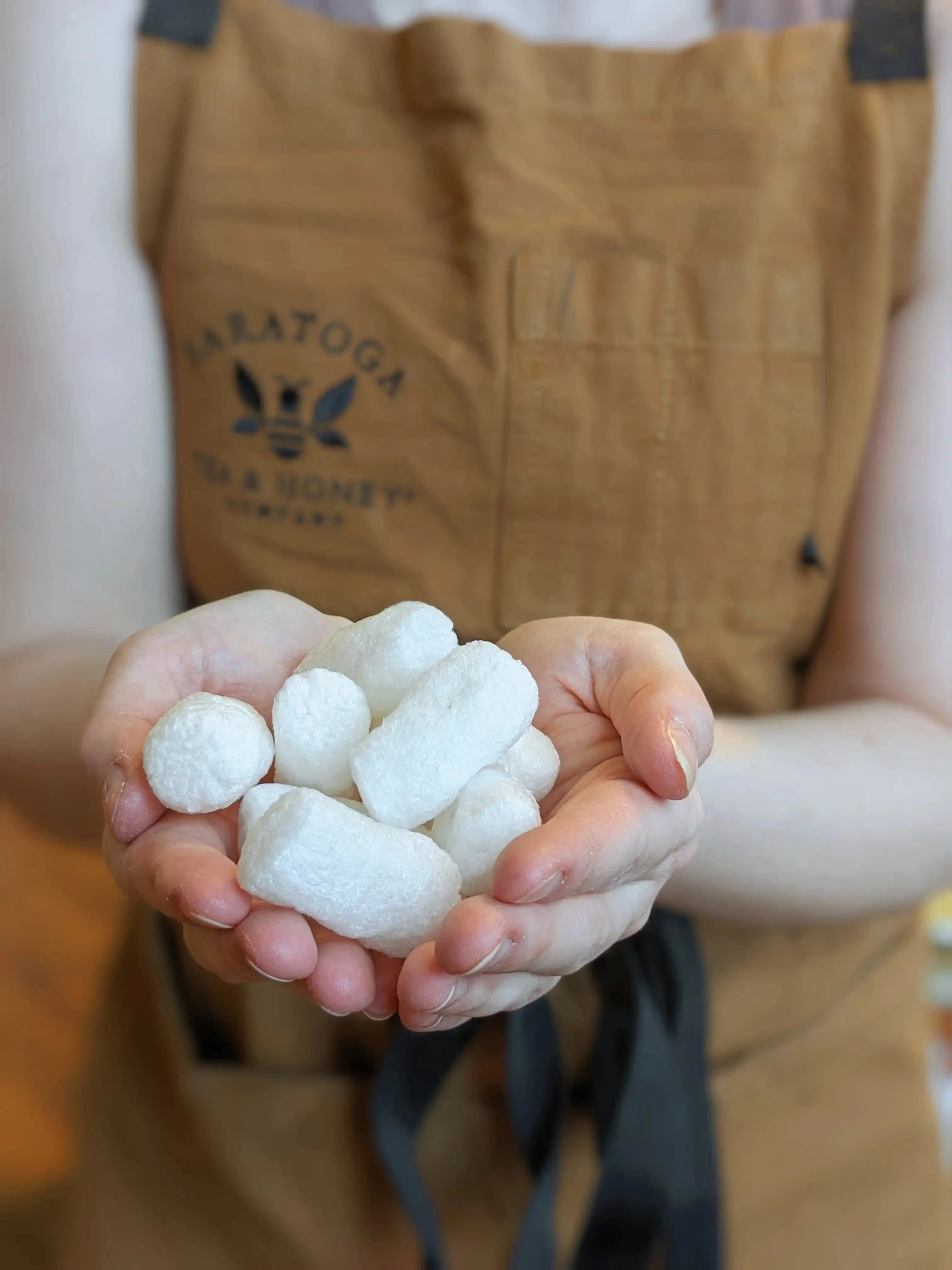 hands cupping a pile of biodegradable packing peanuts in front of a Saratoga Tea & Honey Co. staff apron