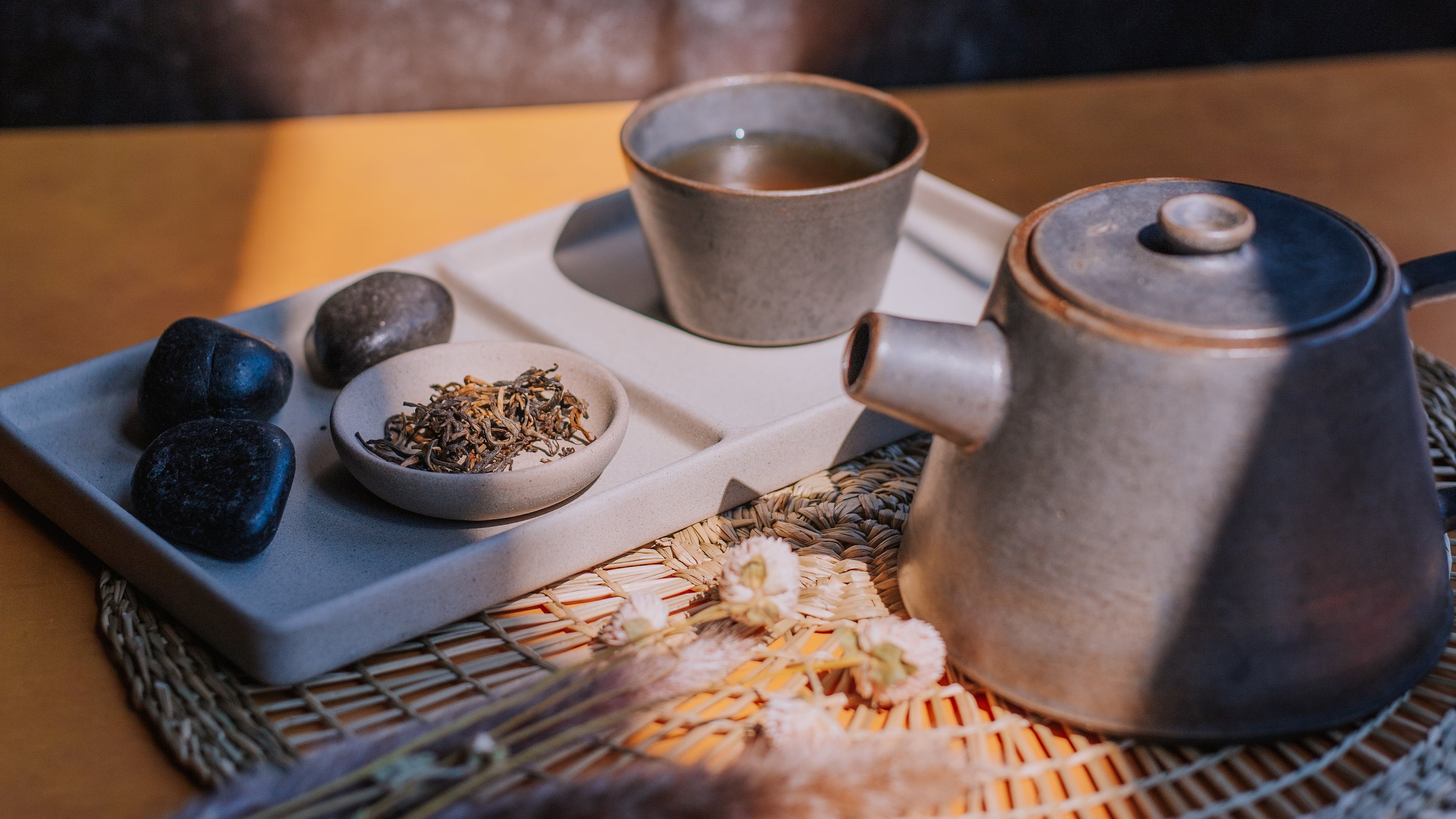 sun illuminating vignette of a clay teapot in foreground with loose leaf tea and cup of tea in the background