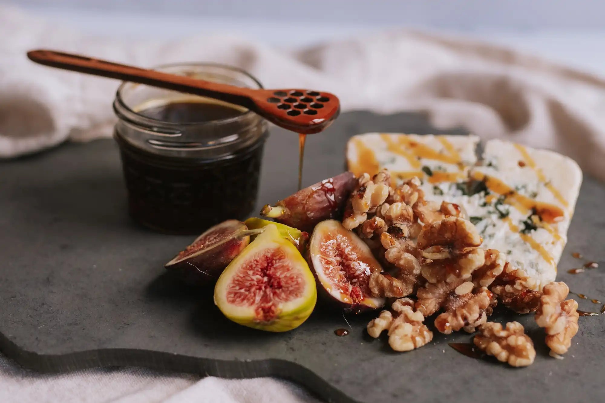 buckwheat honey dripping onto a charcuterie board with figs, walnuts, and cheese