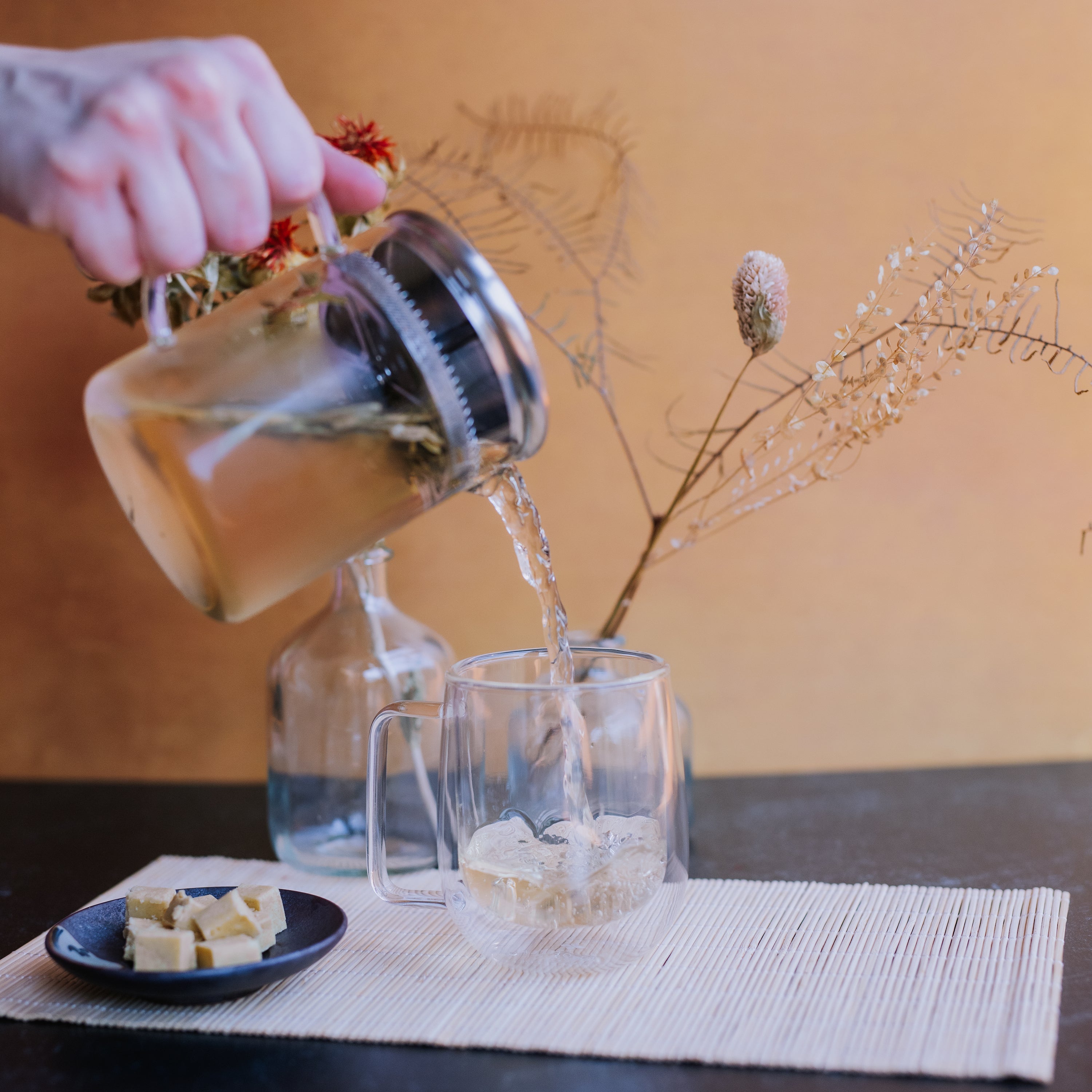 hand pouring green tea from a glass beaker infuser into glass mug