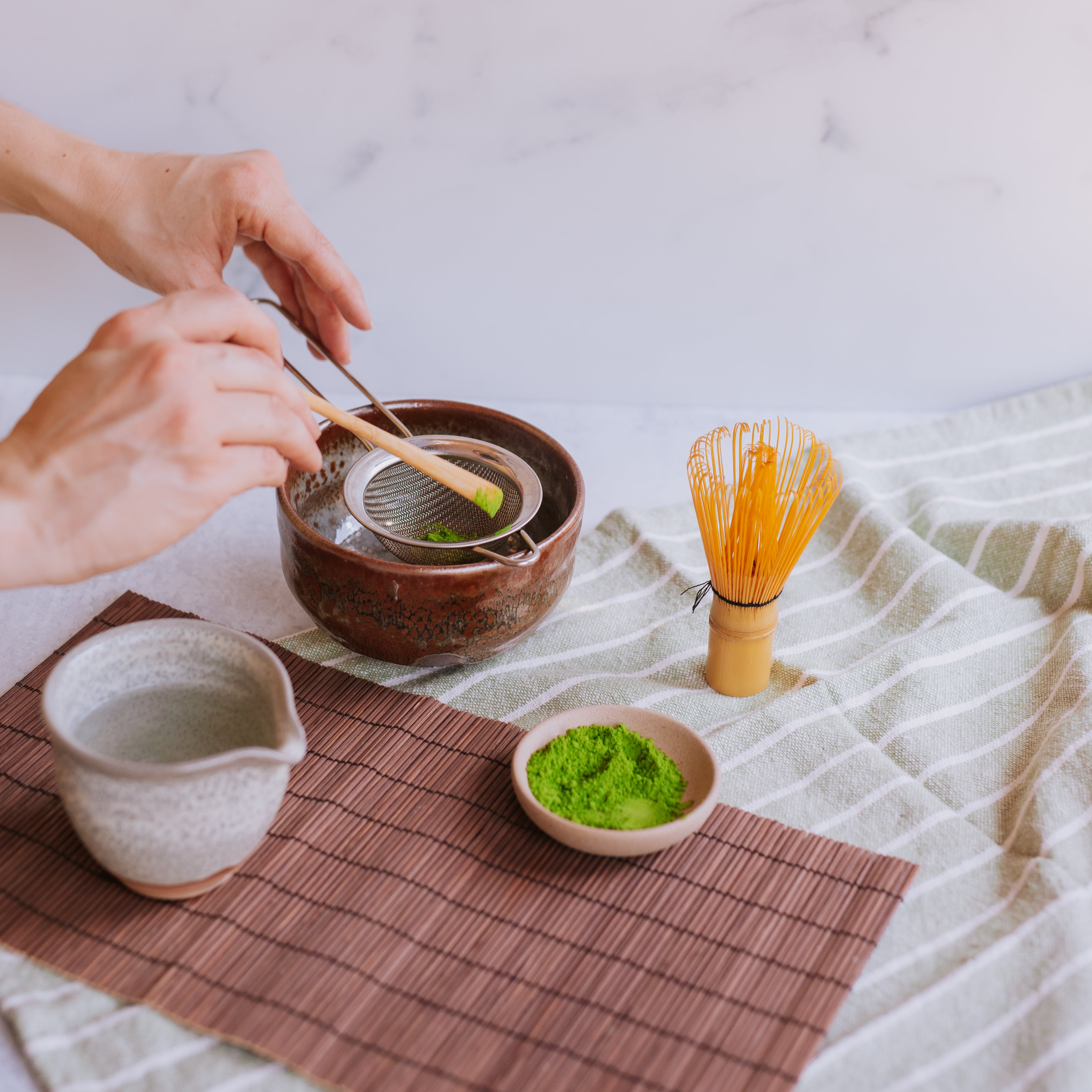 two hands measuring matcha into a matcha bowl with a bamboo scoop in preparation to make matcha