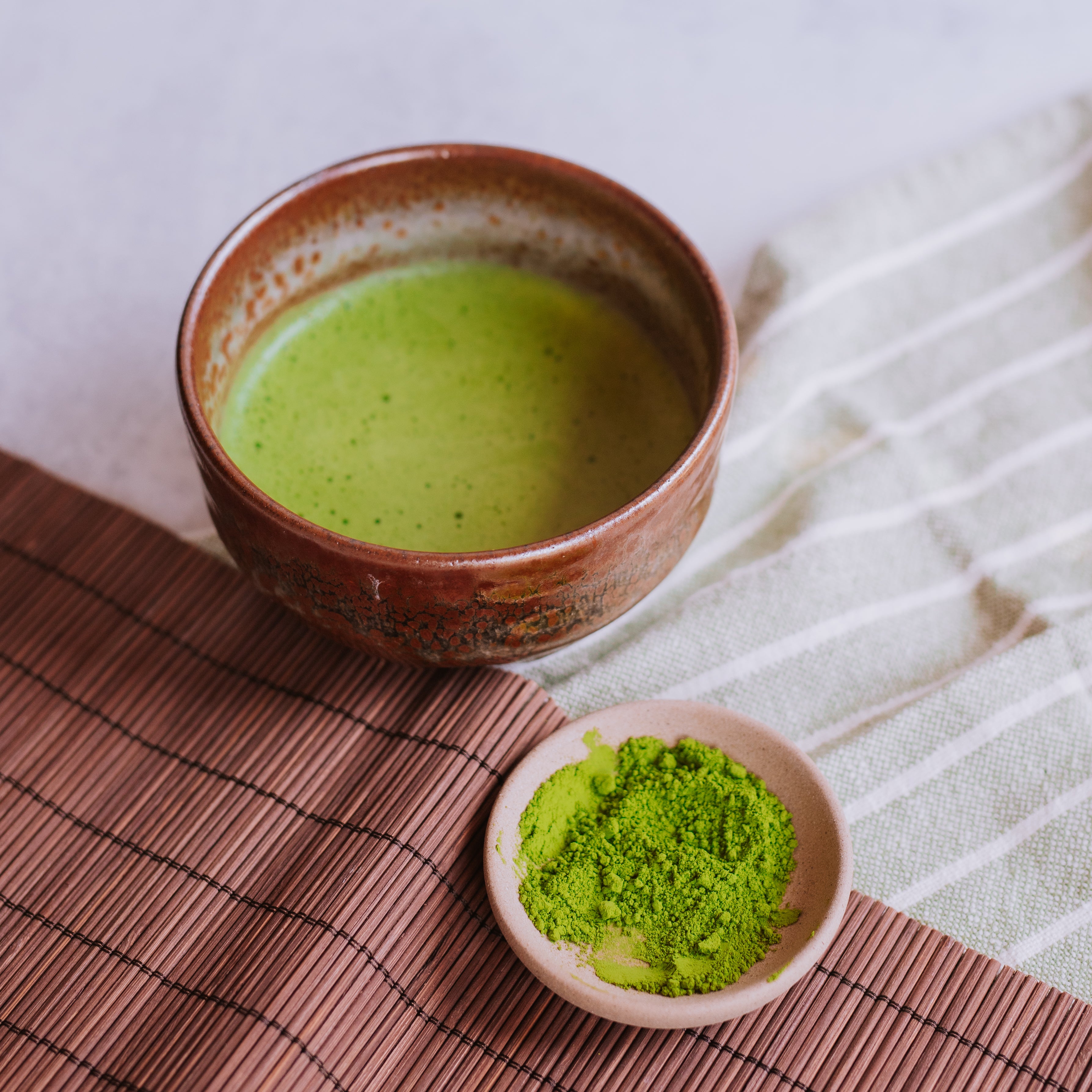 hand thrown earthen ware matcha bowl with frothy matcha side by side with a dish of matcha powder