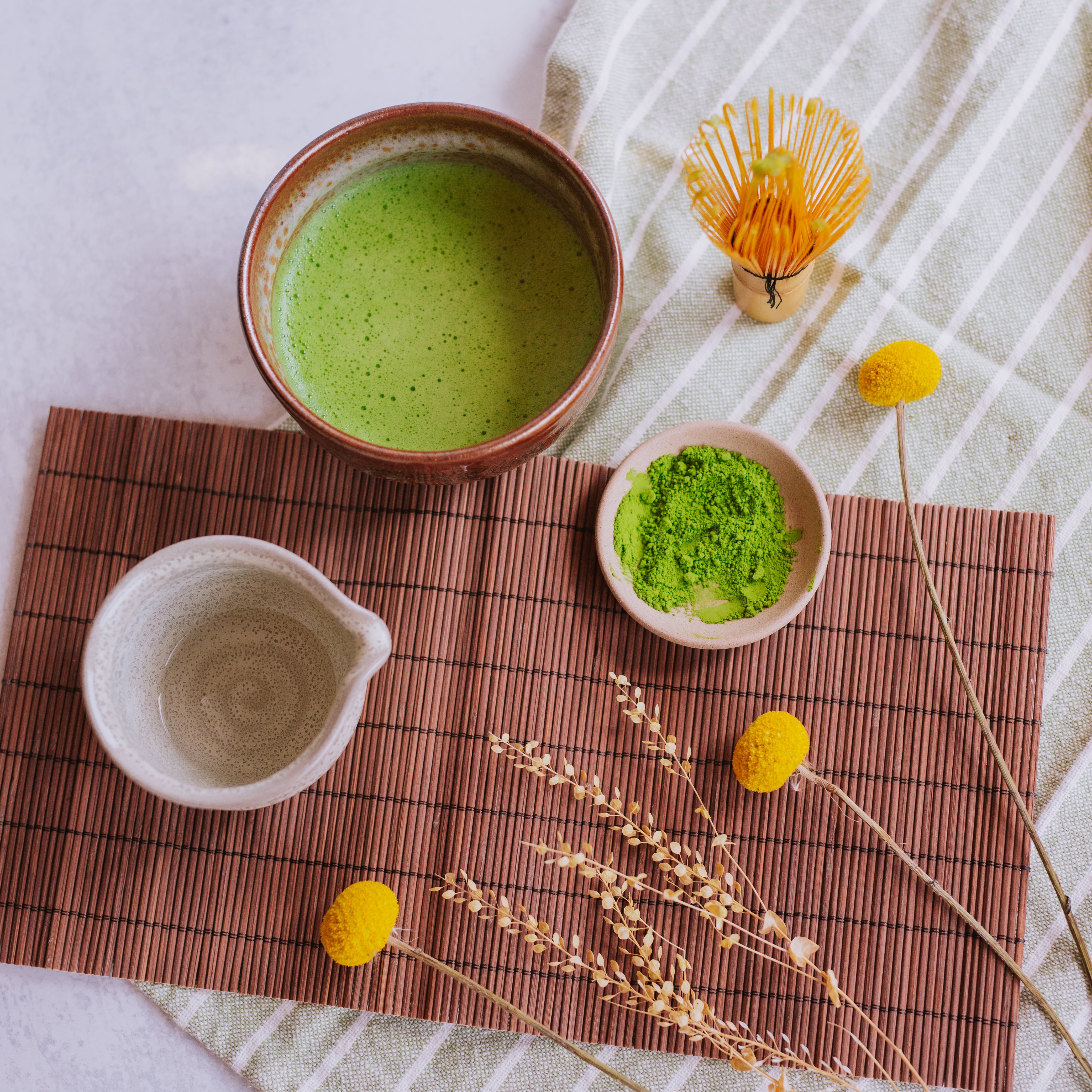 bright green bowl of ceremonial matcha with accessories and matcha powder