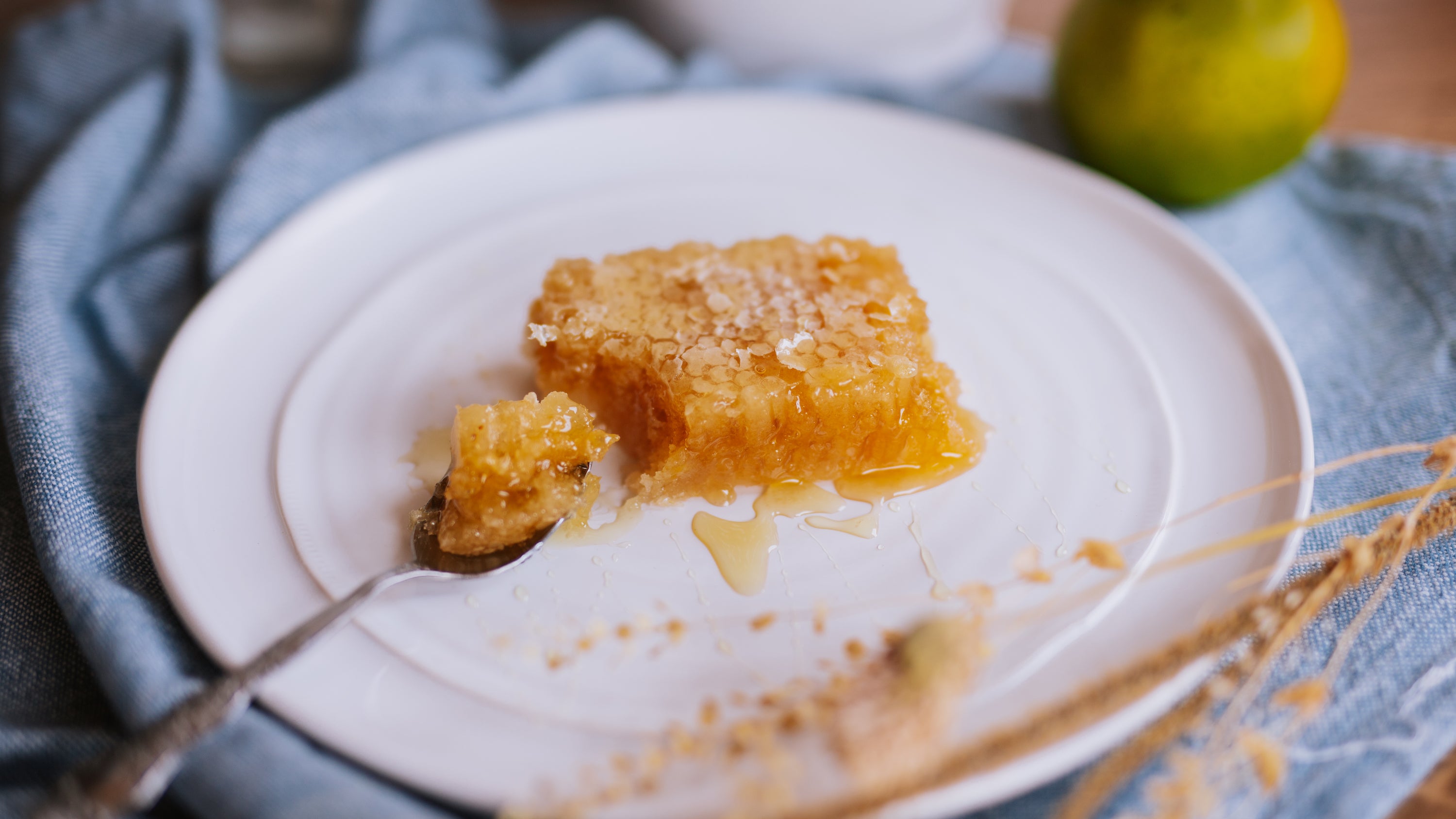 white plate on blue linens with golden acacia honeycomb and spoon with a chunk of comb