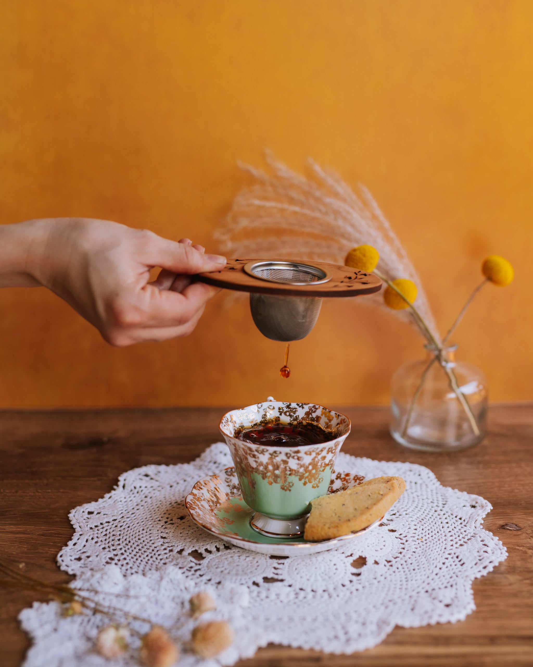 hand holding dripping wooden moonspoon tea strainer over full vintage teacup of black tea