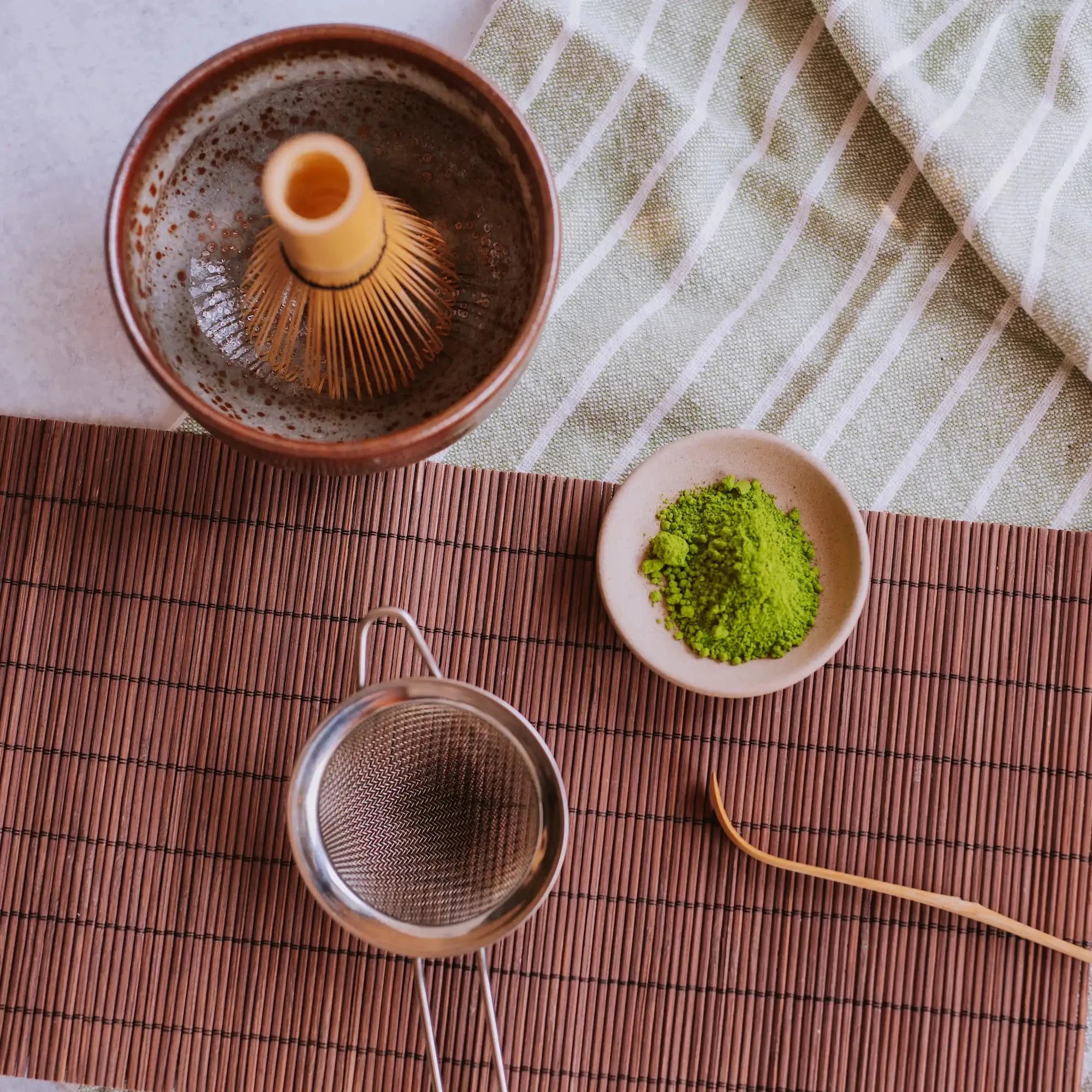 aerial view of matcha bowl with whisk, dish of matcha powder, sieve, and chashaku
