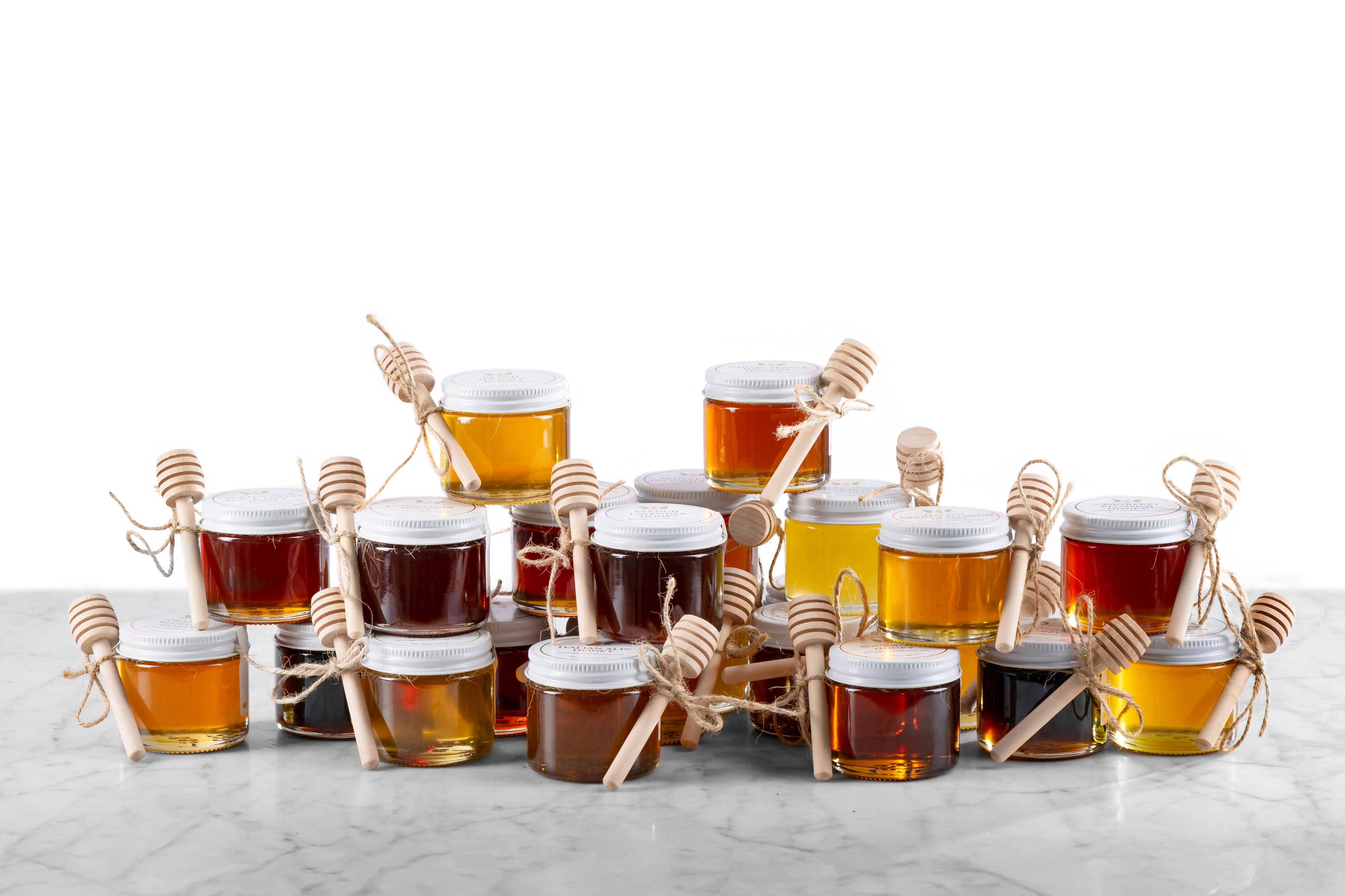 pile of varied stocking stuffer mini honey jars with twine and dipper on a marble surface with white background