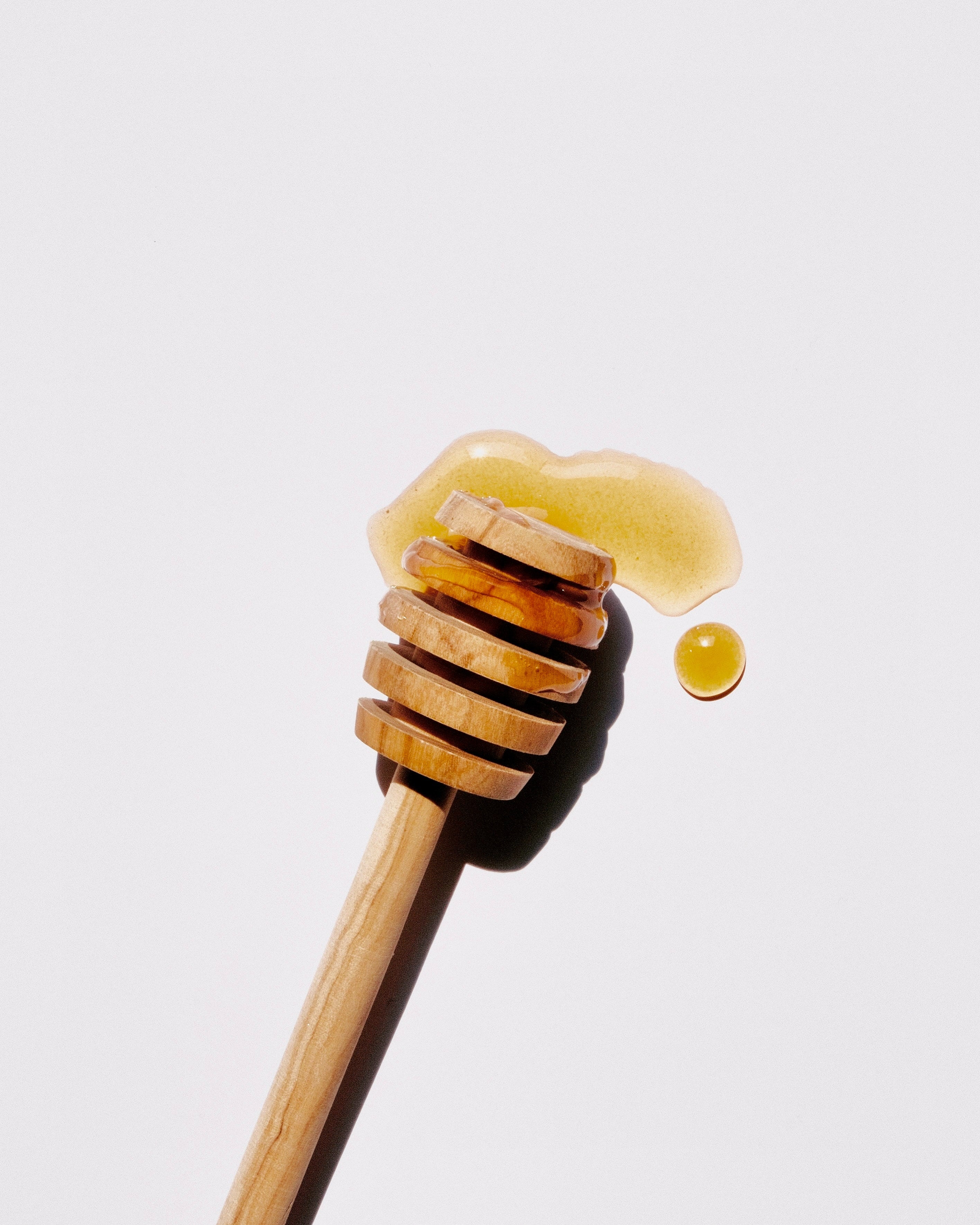wooden honey dipper laid in pool of honey on a white background