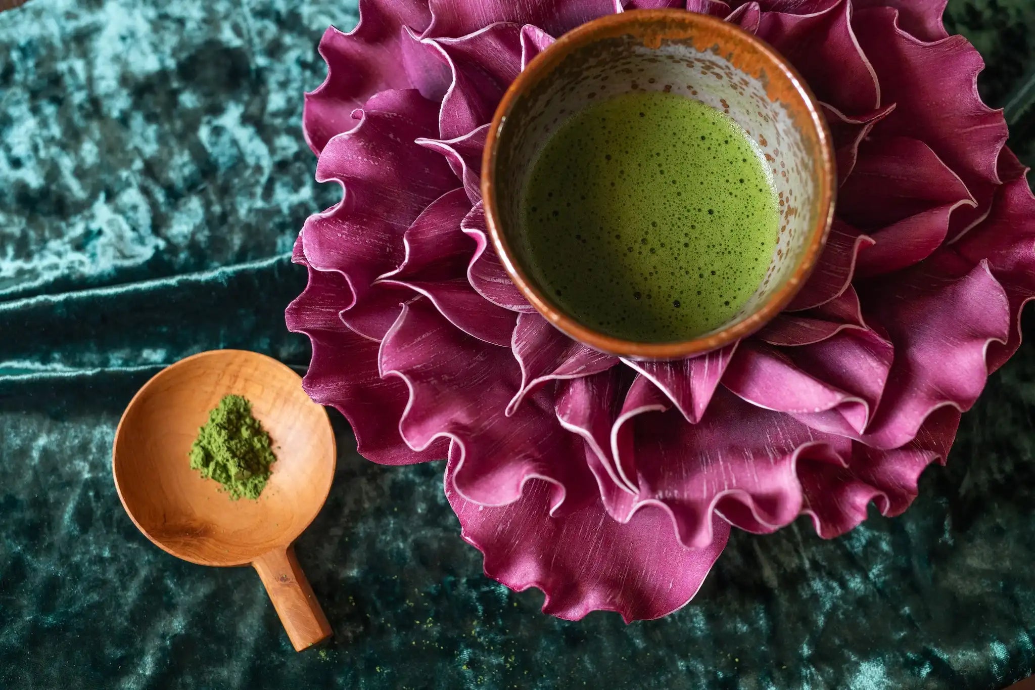 bowl of matcha inside a purple flower and a small wooden serving spoon with bright green matcha powder