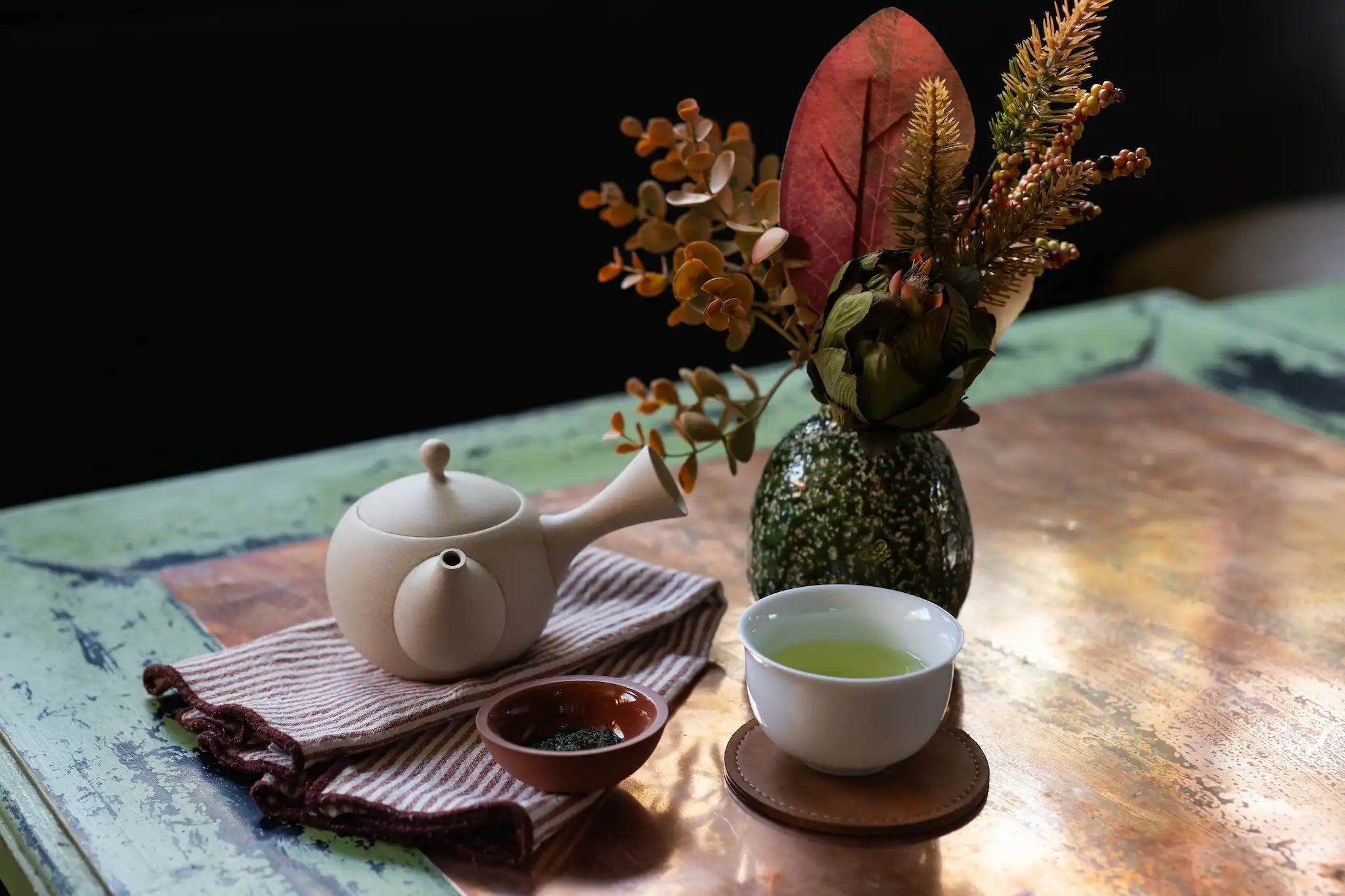 sencha green tea brewed in a kyusu Japanese tea pot and served in a white cup next to a vase with autumn protea