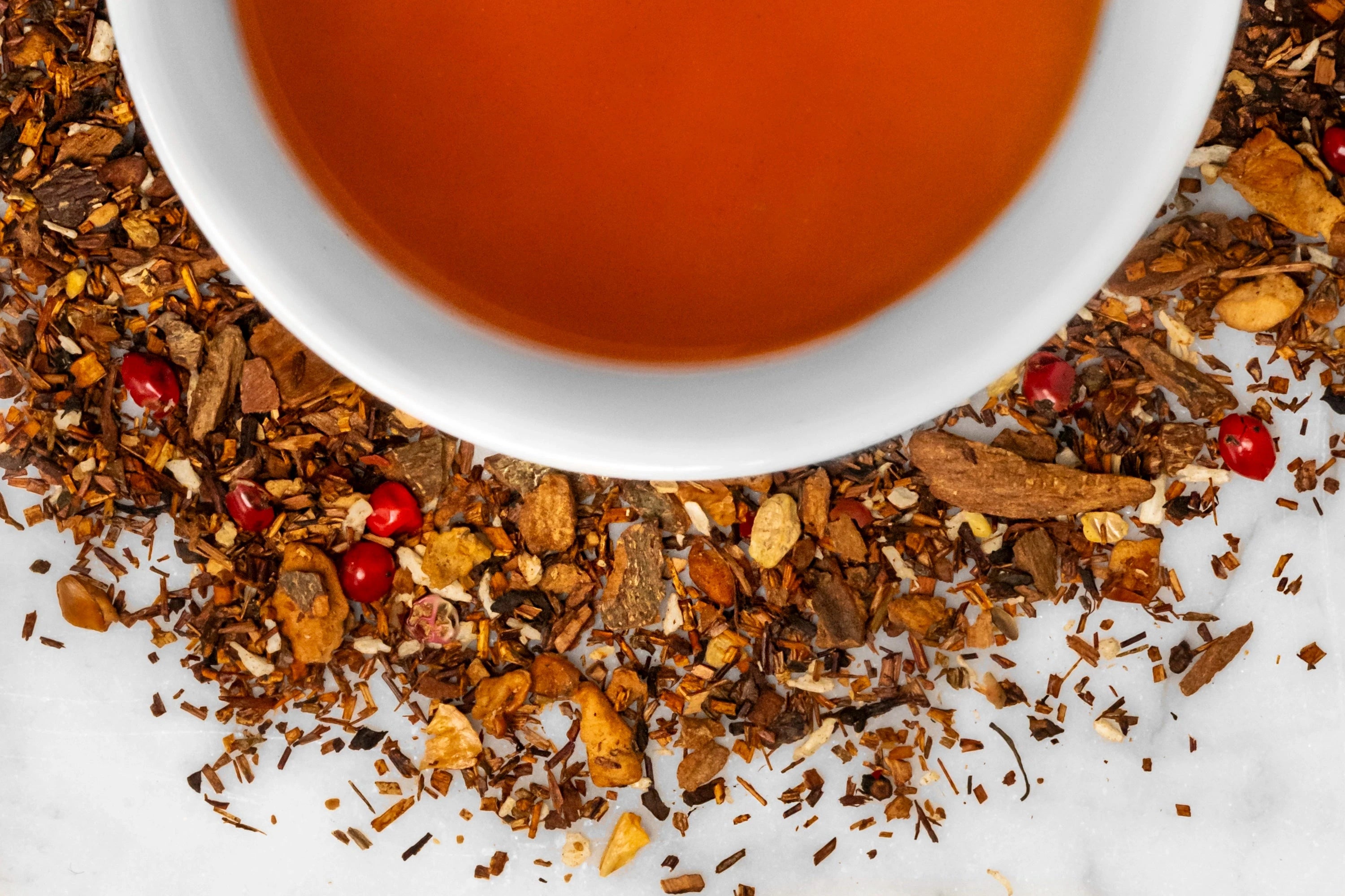 Upstate Apple dry and brewed herbal tea. A mixture of rooibos, cinnamon, pink peppercorn and other herbs and spices surround a cup of reddish-brown brewed tea.