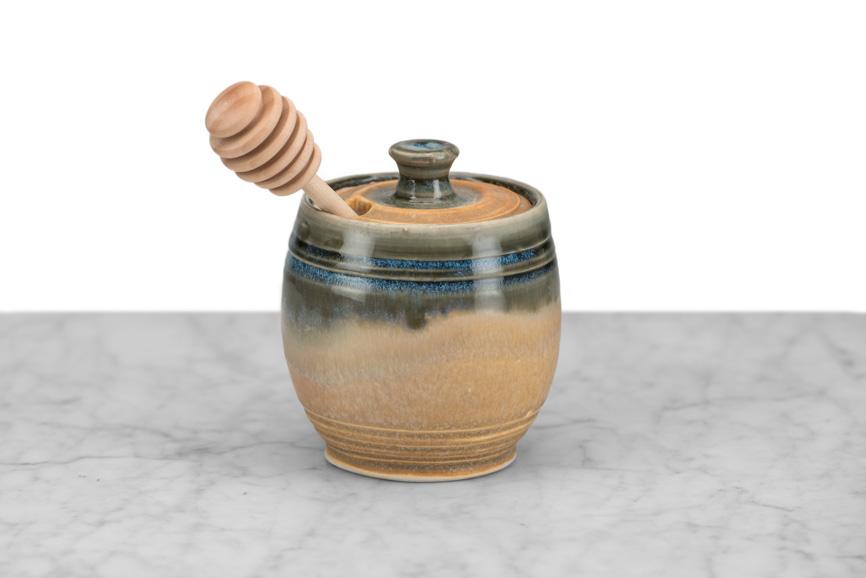 tan honey pot with wooden honey dipper on a marble and white background