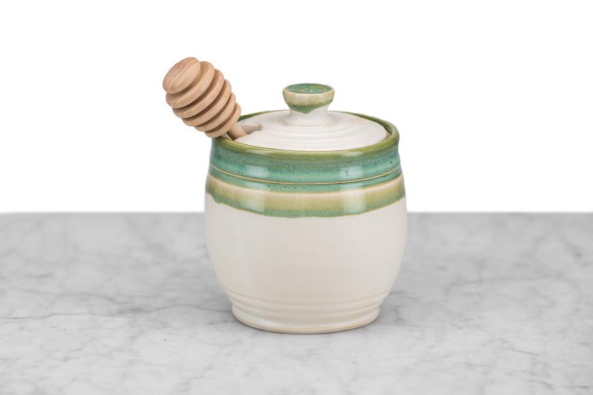 white and mint green clay honey pot with a wooden honey dipper on a marble and white background