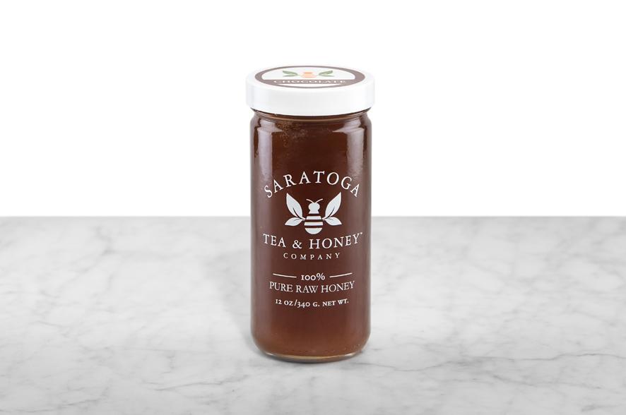 Dark brown Chocolate Infused Honey displayed in a 12oz cylindrical glass jar with a white lid. The logo and the words: "100% Pure Raw Honey" are printed on the jar.