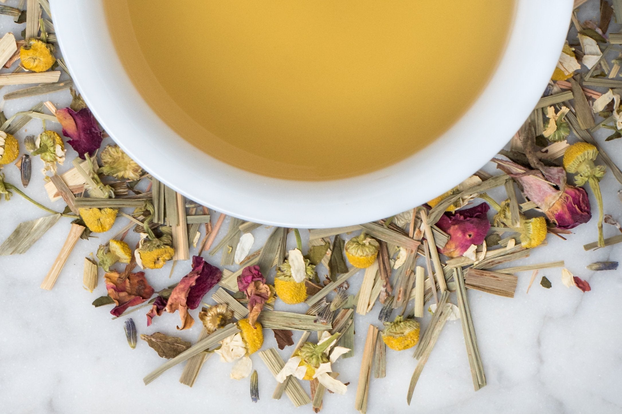 Field of Dreams leaves and brewed tea. A colorful medley of lemongrass, chamomile, peppermint, rose and lavender buds surrounds a cup of straw-hued brewed tea.