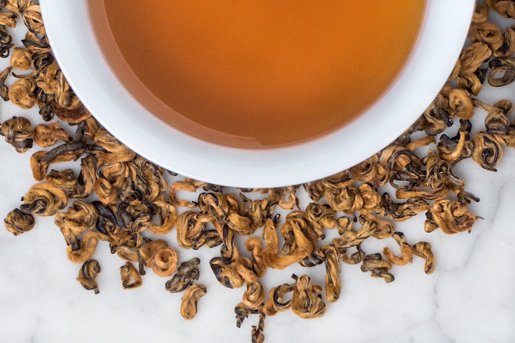 Rolled Gold Black Butterly Tea, Jin Die, Surrounding A Brewed Burnt Orange Cup