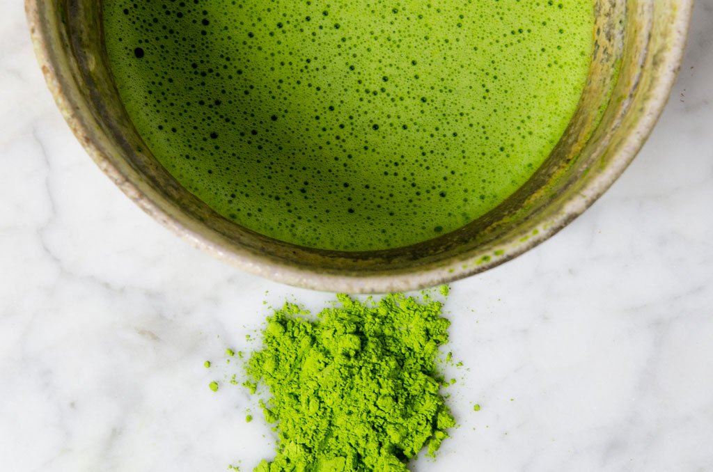 matcha powder next to a traditionally prepared bowl of matcha
