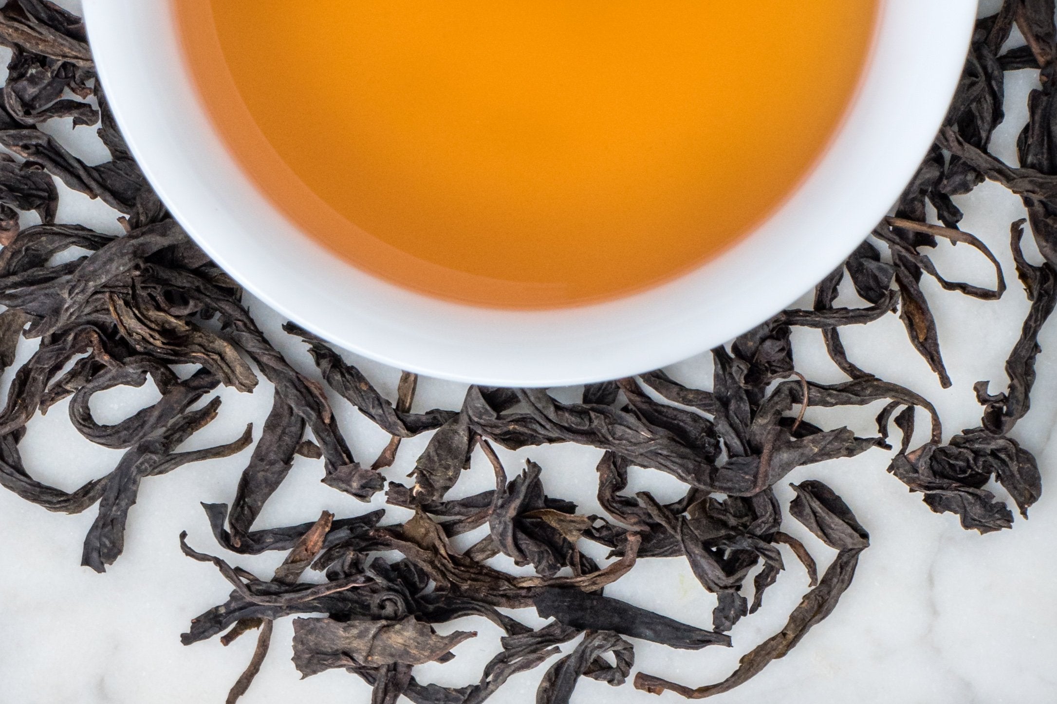 Shui Xian Lao Cong leaves and brewed tea. Large, twisted black leaves surround a cup of russet-colored brewed oolong tea.