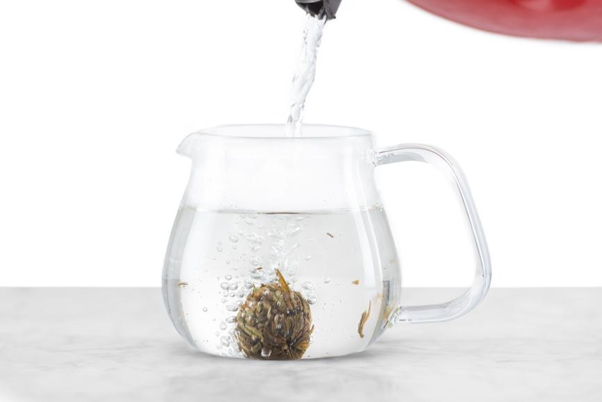 Jasmine Flower Craft tea ball brewing - stage one. Water is poured over unopened, hand-tied green tea ball resting on the bottom of a glass teapot.