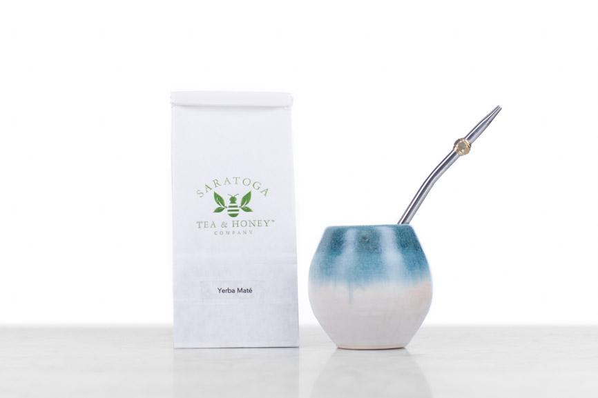 bag of yerba mate sitting next to a clay yerba mate gourd with a metal bombilla