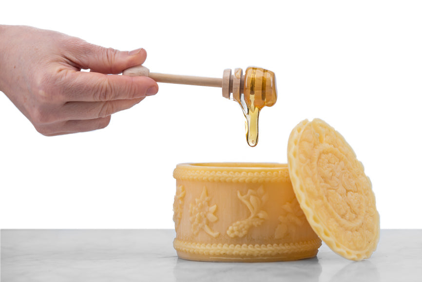 hand dripping honey into a beeswax honey pot on a marble and white background