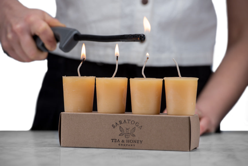 woman lighting four beeswax votives with a long-necked grill lighter