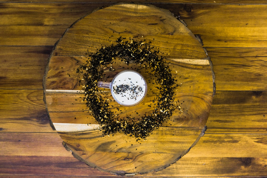chai latte surrounded by loose leaf masala chai tea leaves on a wood background