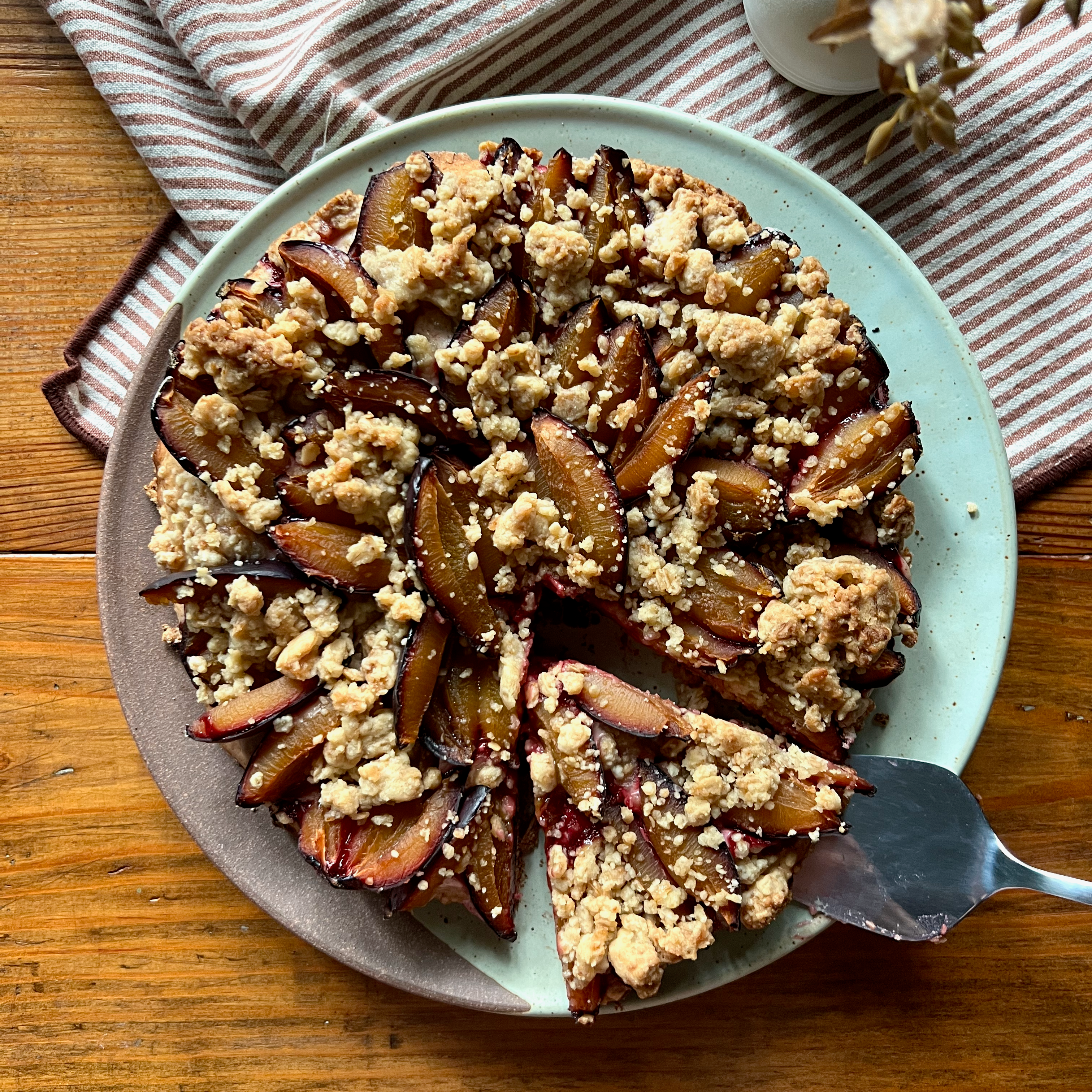 round German plum cake with streusel topping with one triangular piece cut out and a serving slicer