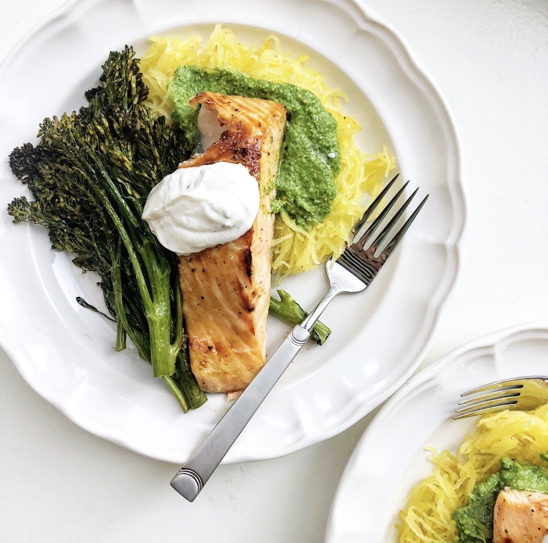 pan seared salmon filets over a bed of spaghetti squash with a side of broccolini on a white fluted plate