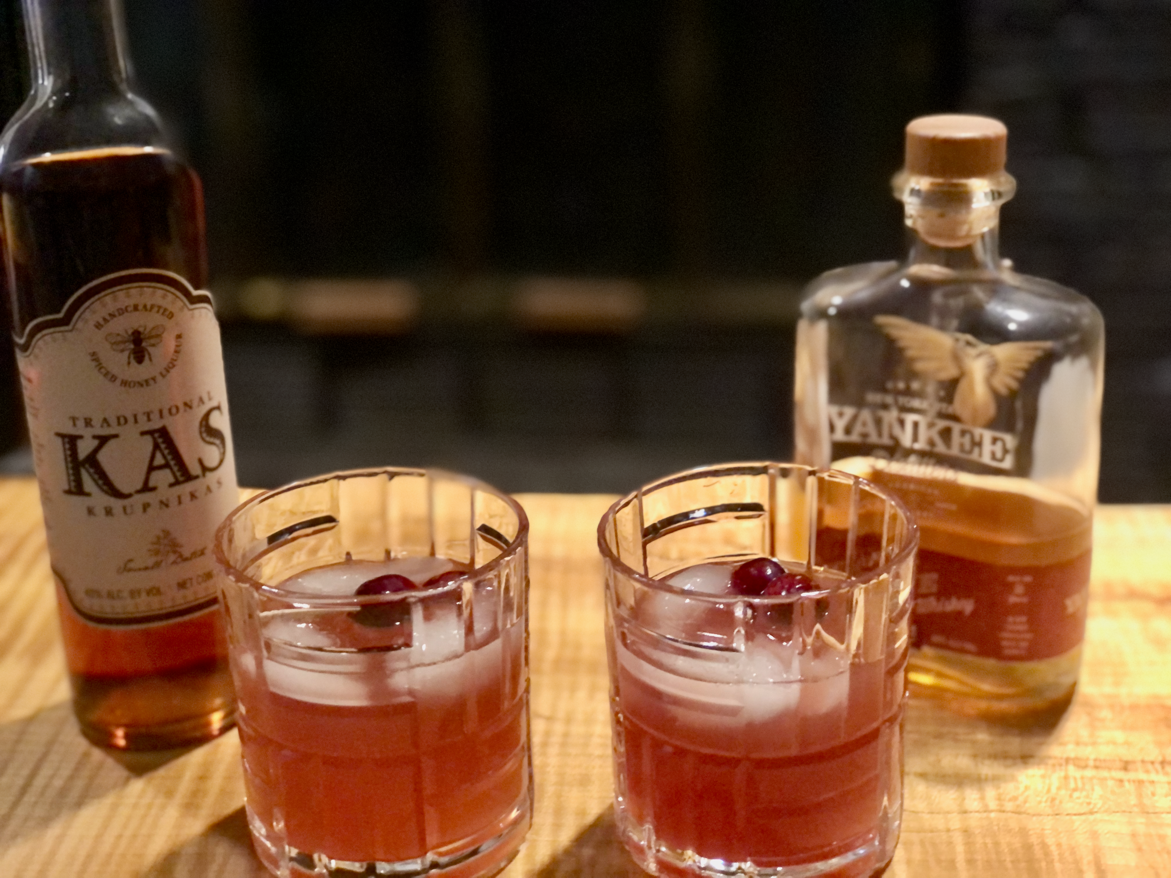 Immune boosting cranberry and pine shrub cocktails in front of Kas honey liquor and Yankee Distillers whiskey bottles