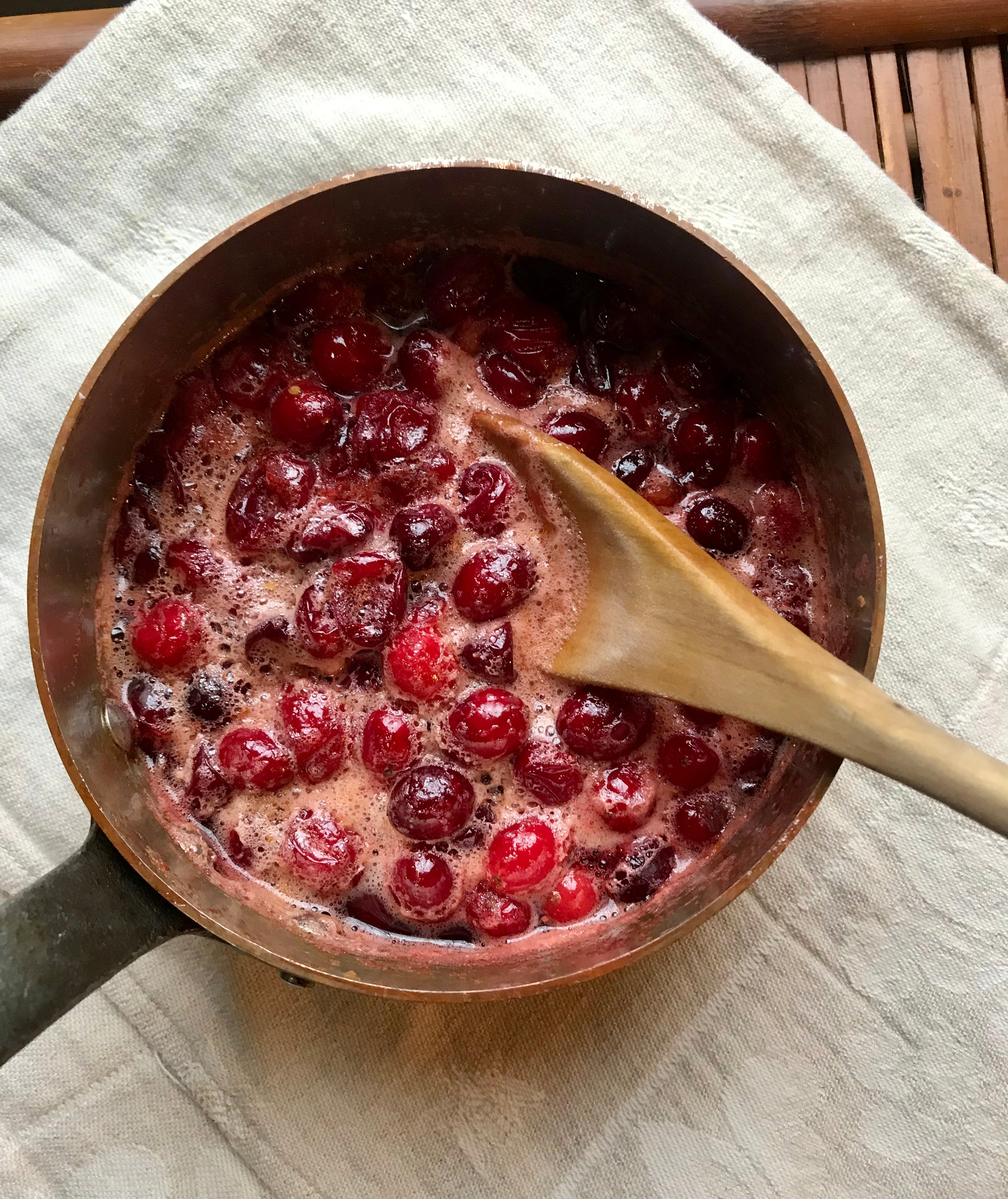 cranberries popping in a copper sauce pan with a wooden spoon
