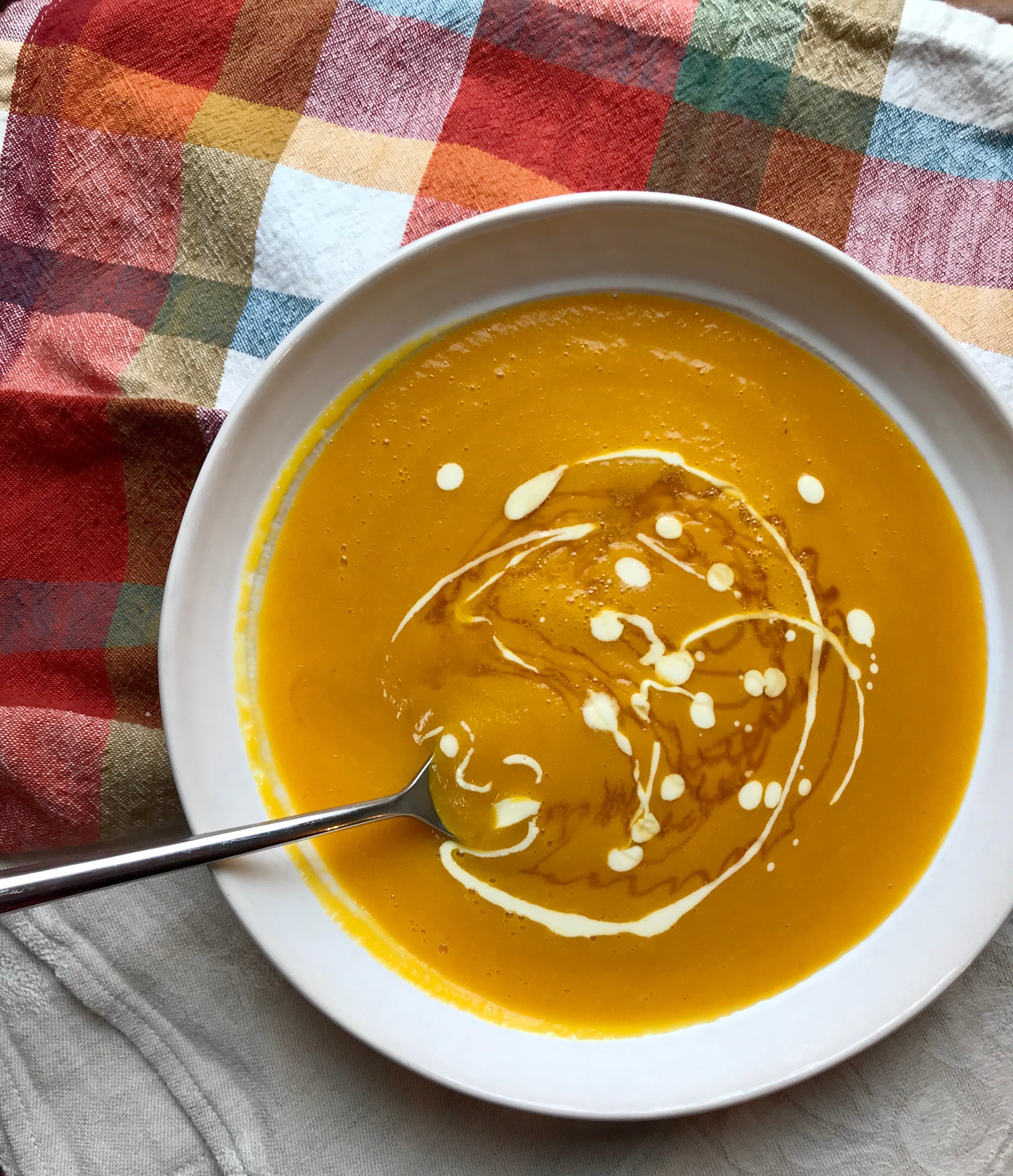creamy orange butternut squash soup in a white bowl with a metal spoon and artistically drizzled yogurt sauce