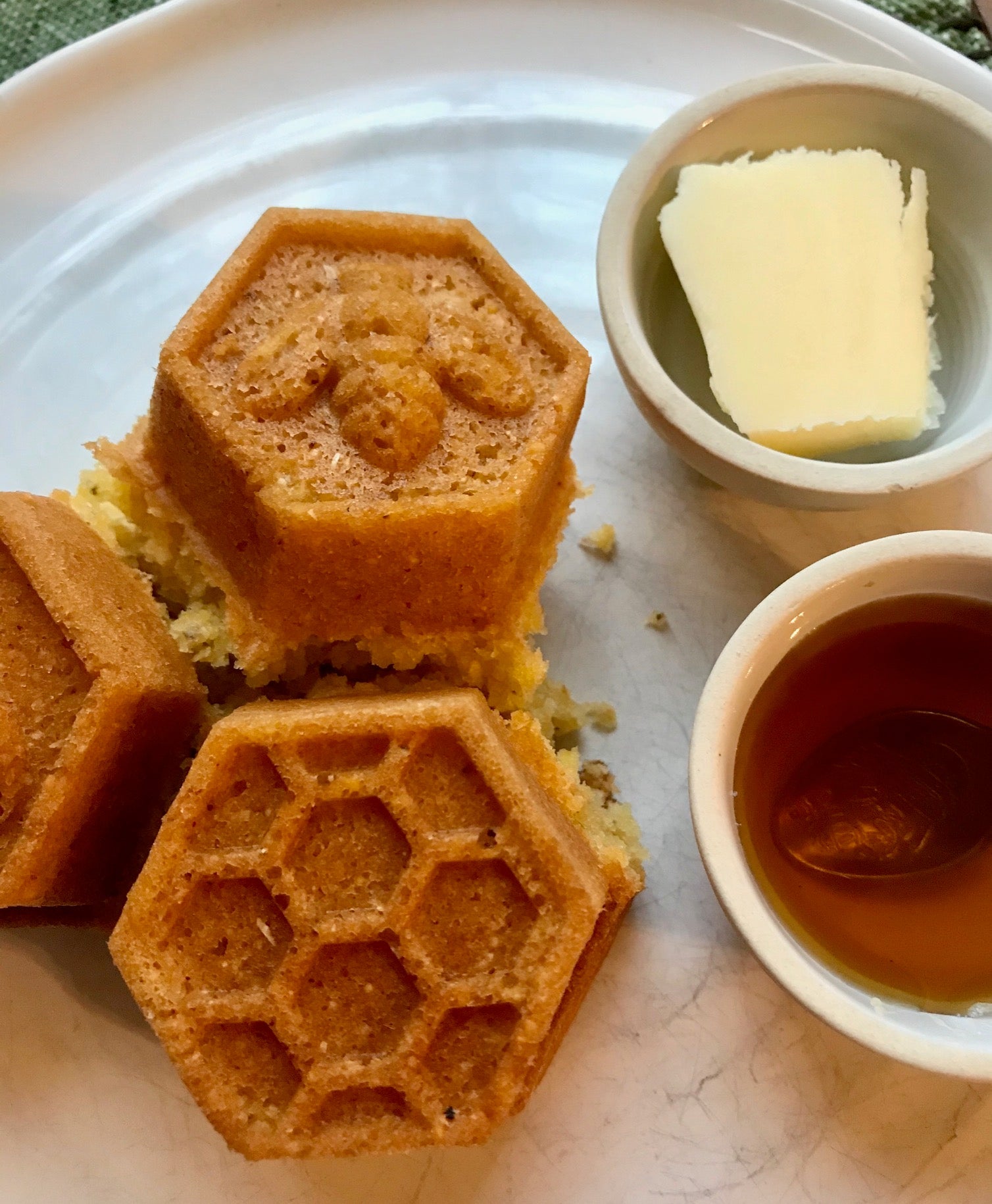cornbread shaped into honeycomb hexagons with bees and honeycomb patterns on a plate next to honey and butter