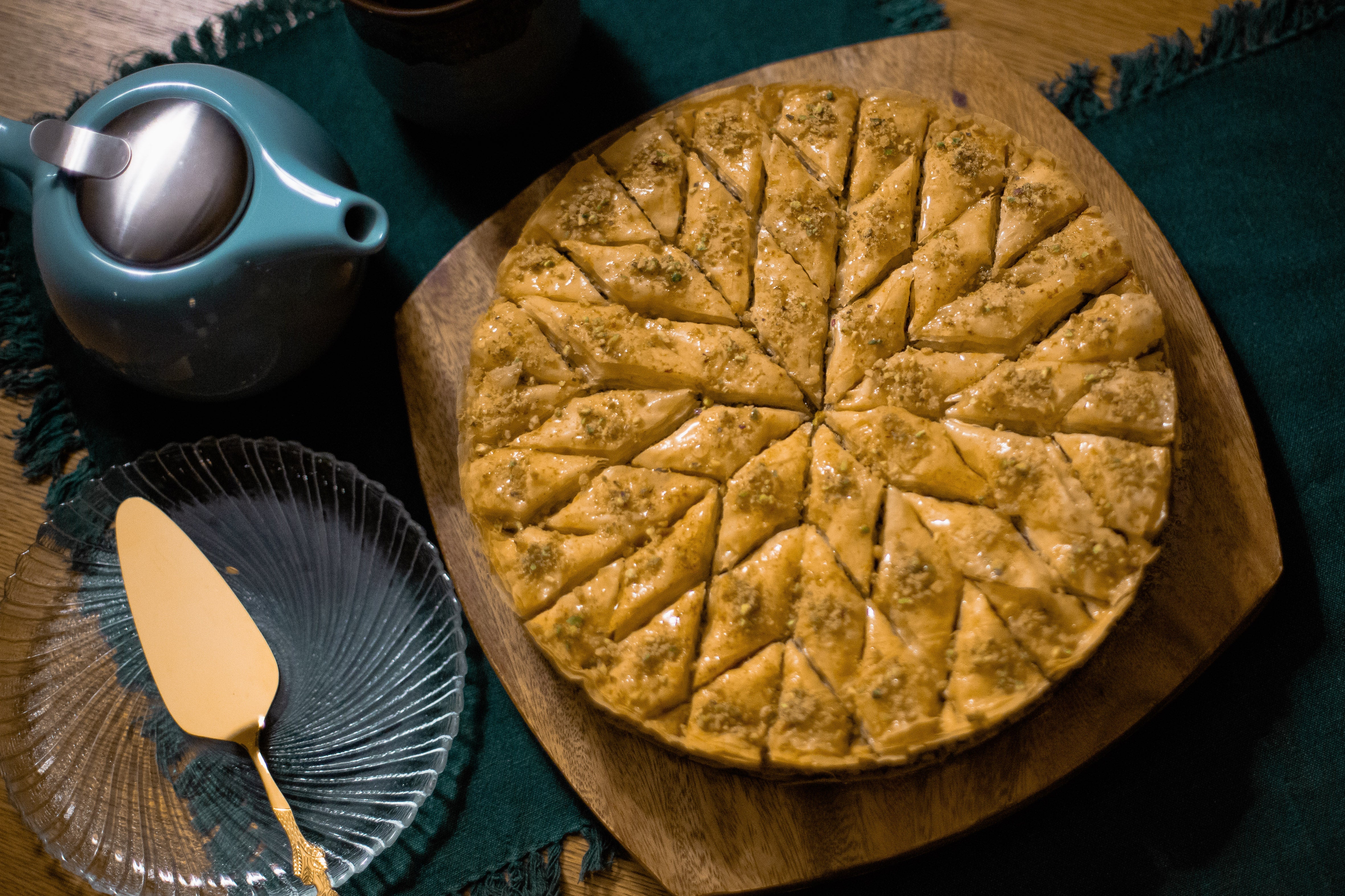 round baklava cut into a star pattern next to a teal teapot and metal pie server