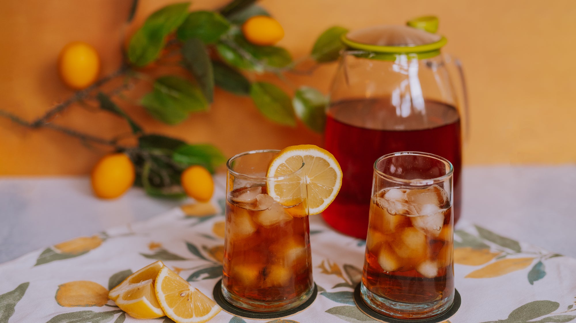 pitcher of black iced tea with two glasses of iced tea and lemon