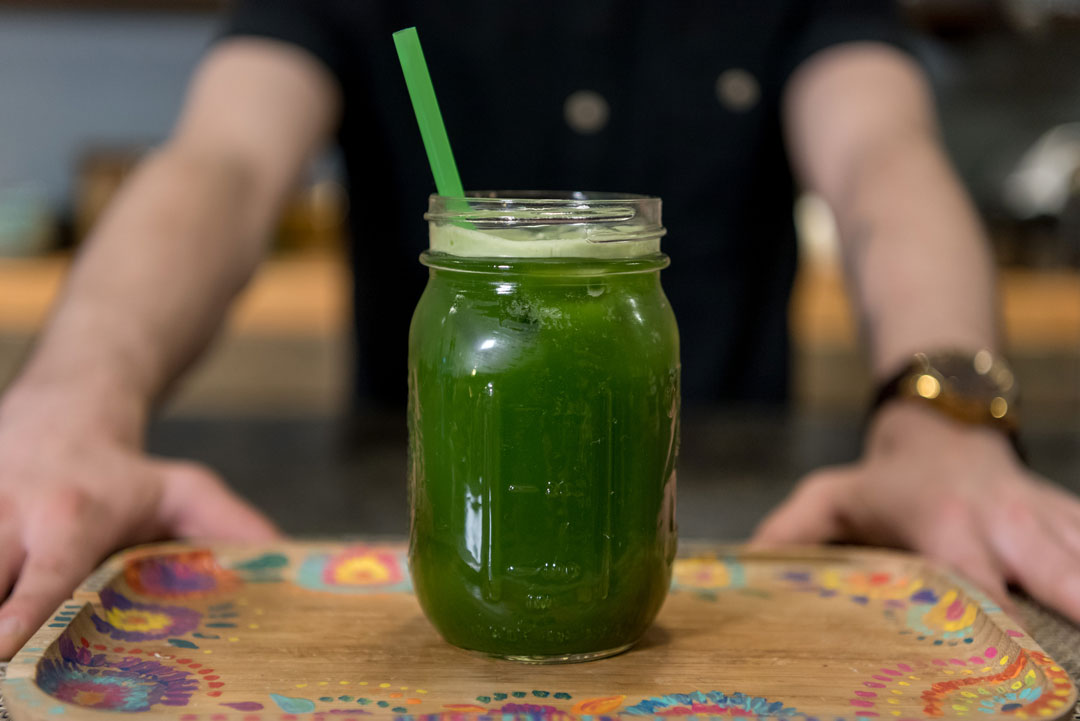 man presenting wooden tray with a mason jar of vibrantly green iced matcha