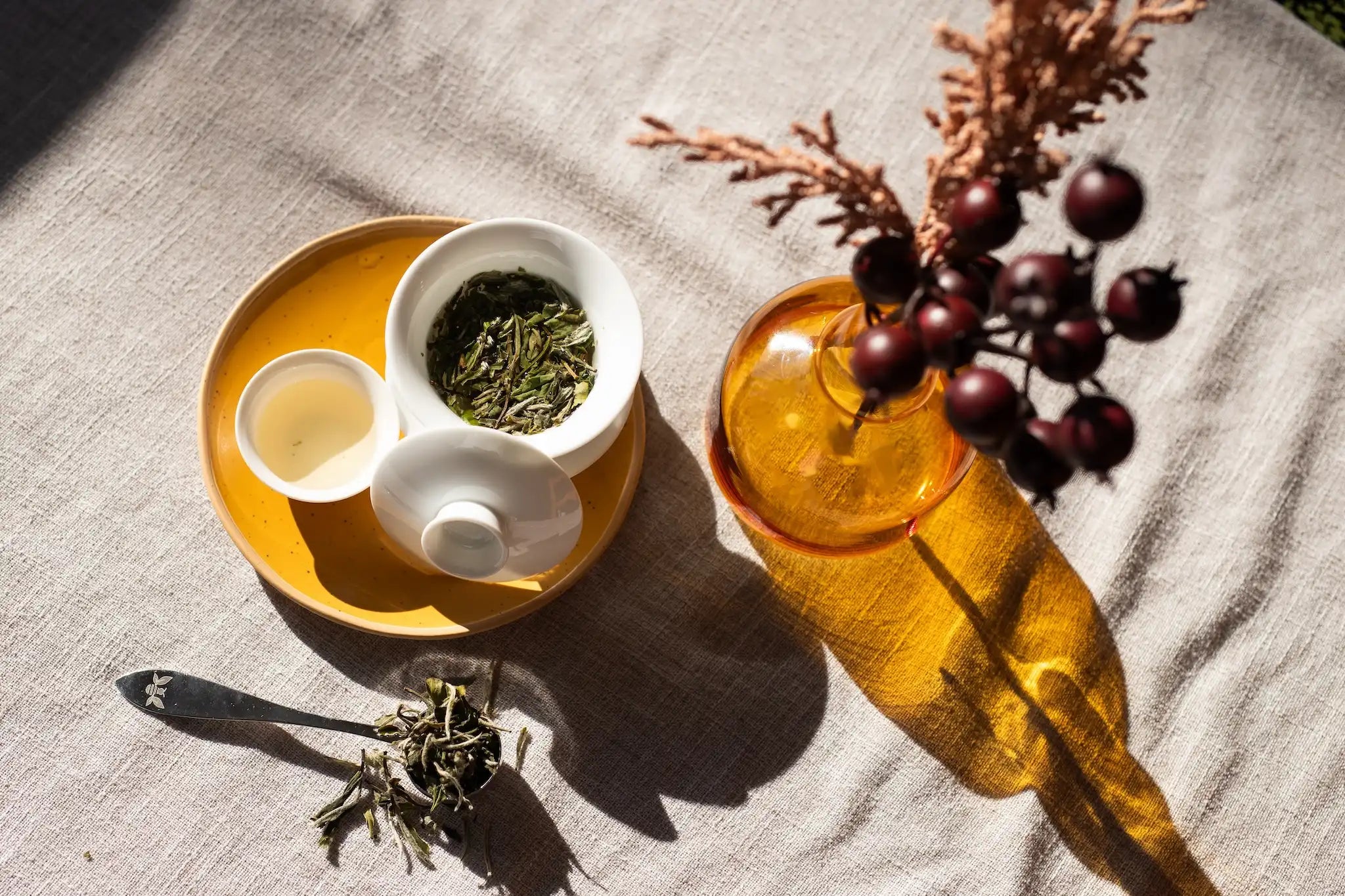 white tea in a gaiwan with a yellow vase of purple flowers