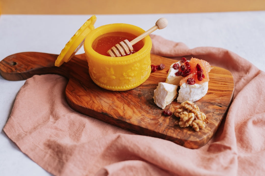 charcuterie board with soft cheese, nuts, and honey in a beeswax honey pot