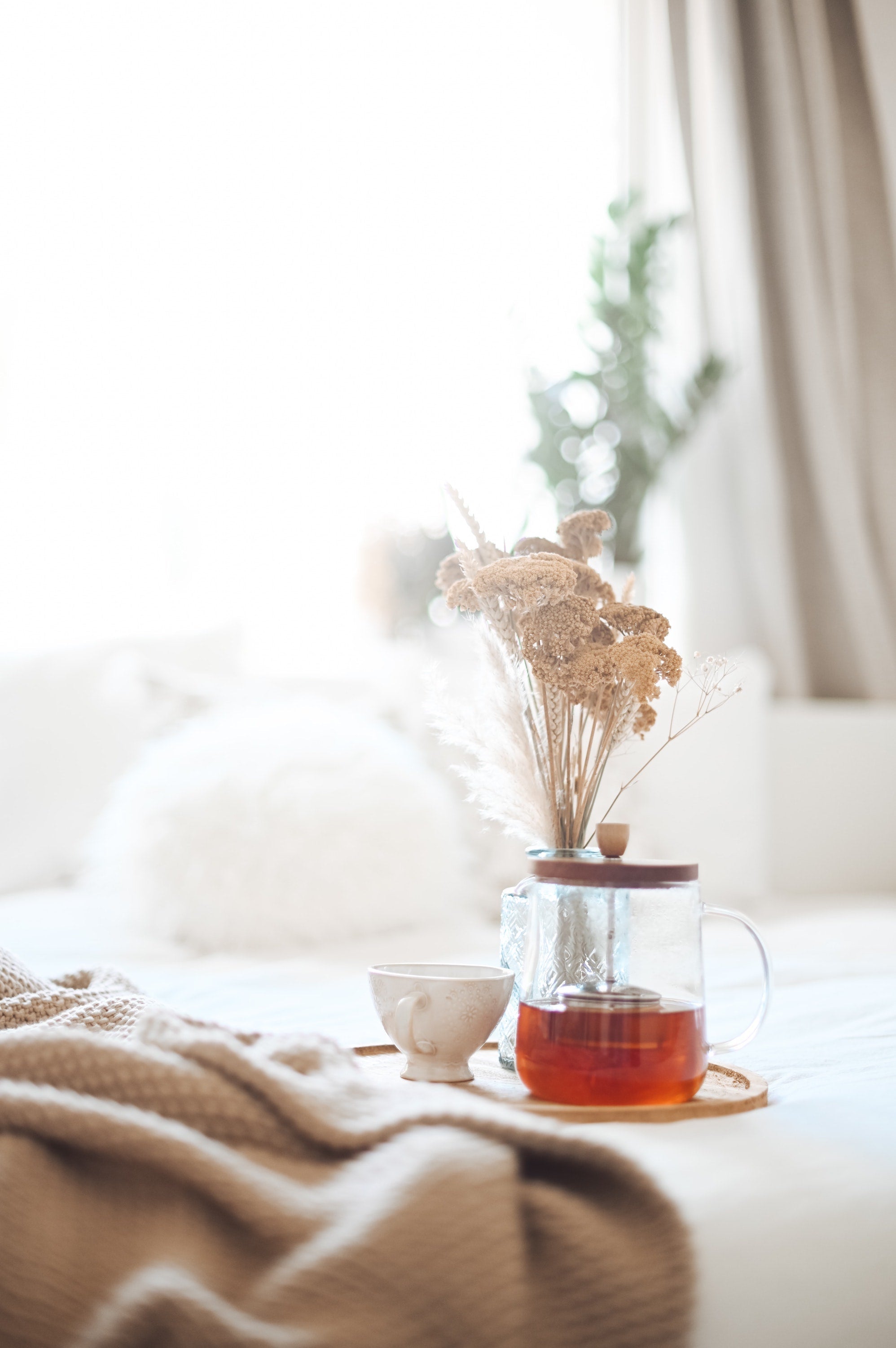calming and muted scene of tea brewing in a glass teapot next to a vintage cup, all set on a cozy blanket