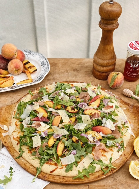 round flatbread with arugula and grilled peaches with grilled peaches and ghost pepper honey in the background
