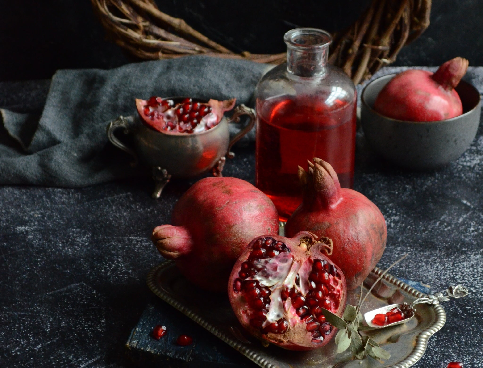 flask of red punch surrounded by pommegranates on a dark background