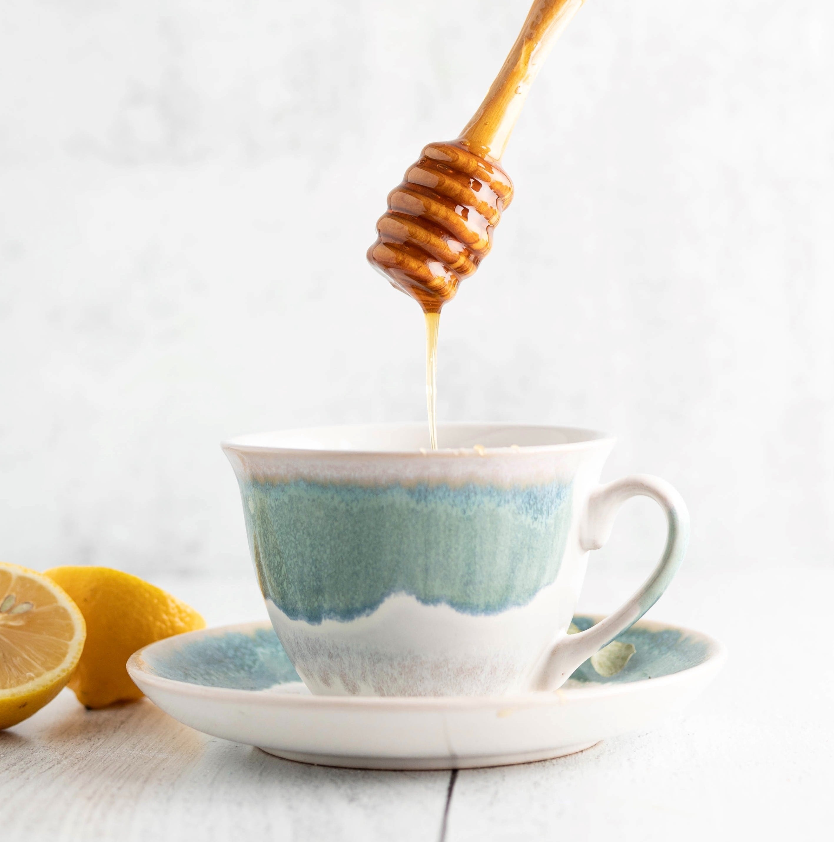 honey dripping into a blue and white teacup from a wooden honey dipper