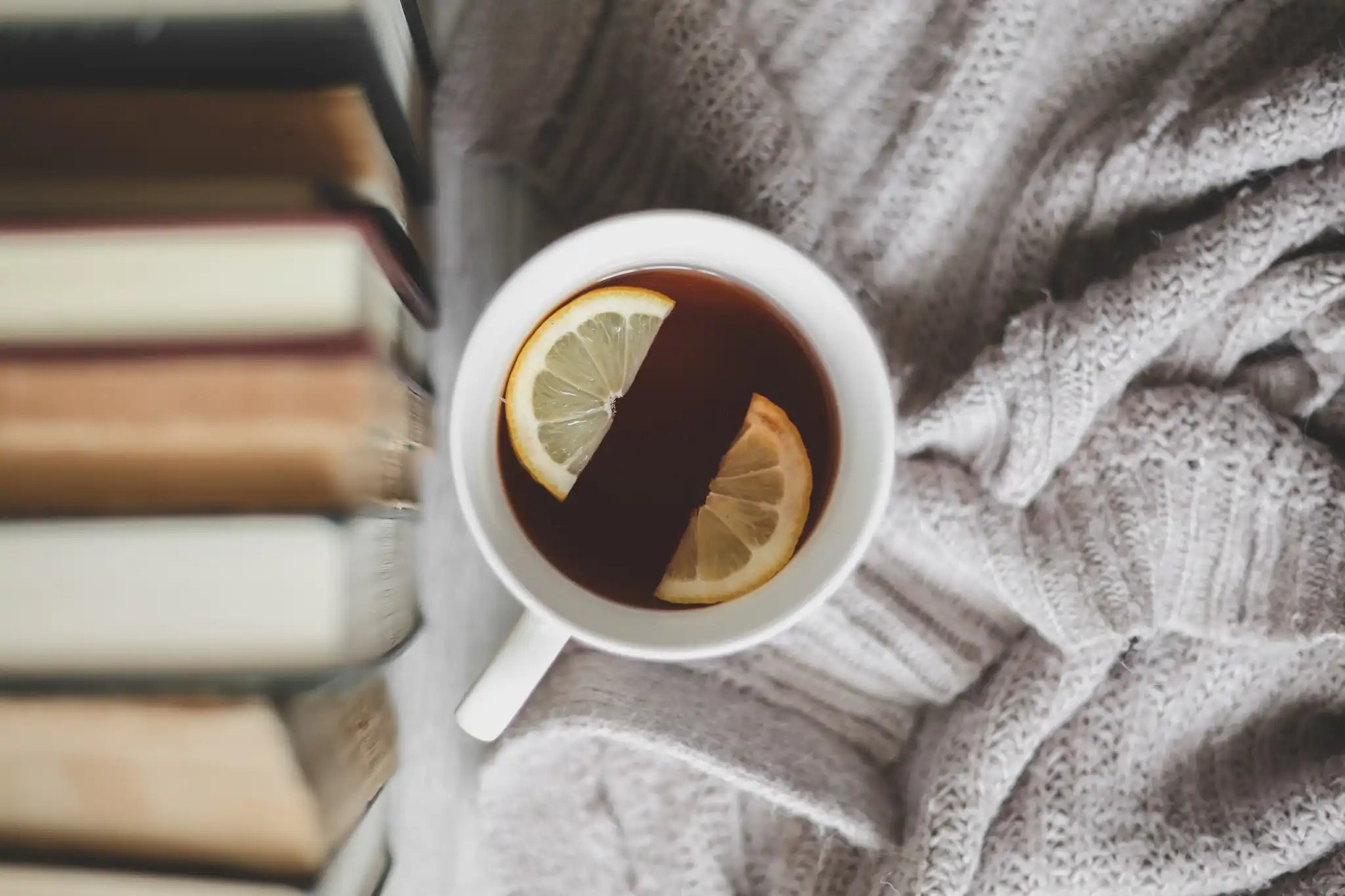 mug of tea with lemons nestled in a blanket next to a stack of books