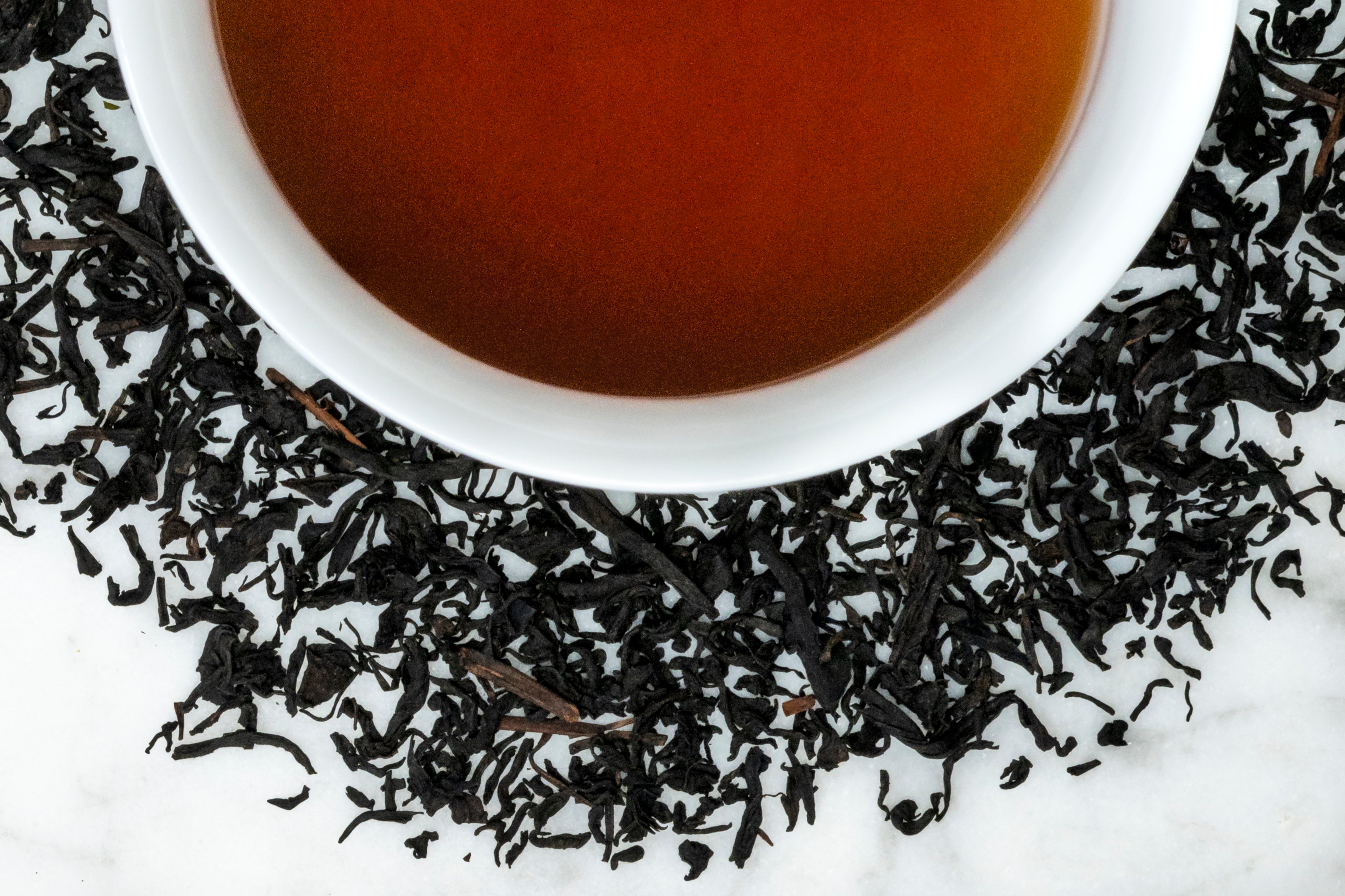 2020 Jeju leaves and brewed tea. Dark brown, almost black twisted leaves of varying sizes and shapes surround a cup of dark reddish-brown brewed pu erh tea.