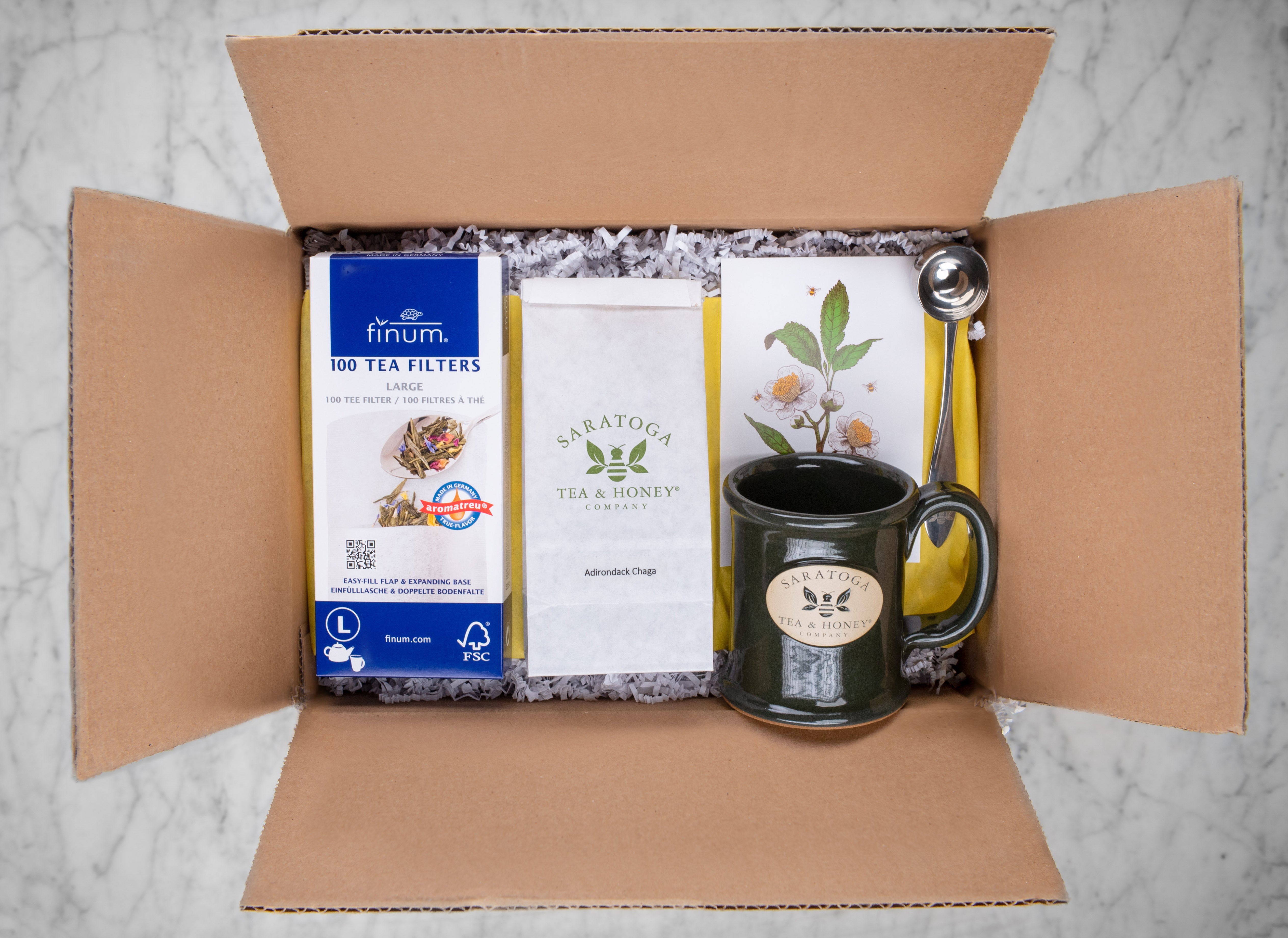 gift box with adirondack themed tea gifts including tea filters, adirondack chaga mushroom tea, saratoga tea and honey branded stoneware mug, gift note, and perfect tea scoop